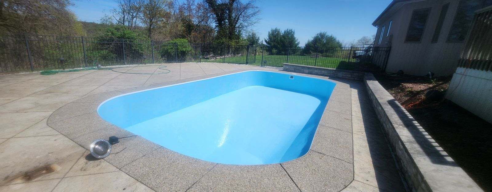 Backyard swimming pool with blue water beside a house on a sunny day