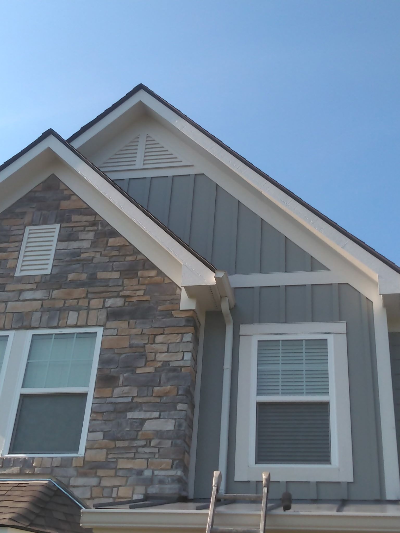 Exterior corner of a house with stone and gray siding under a blue sky