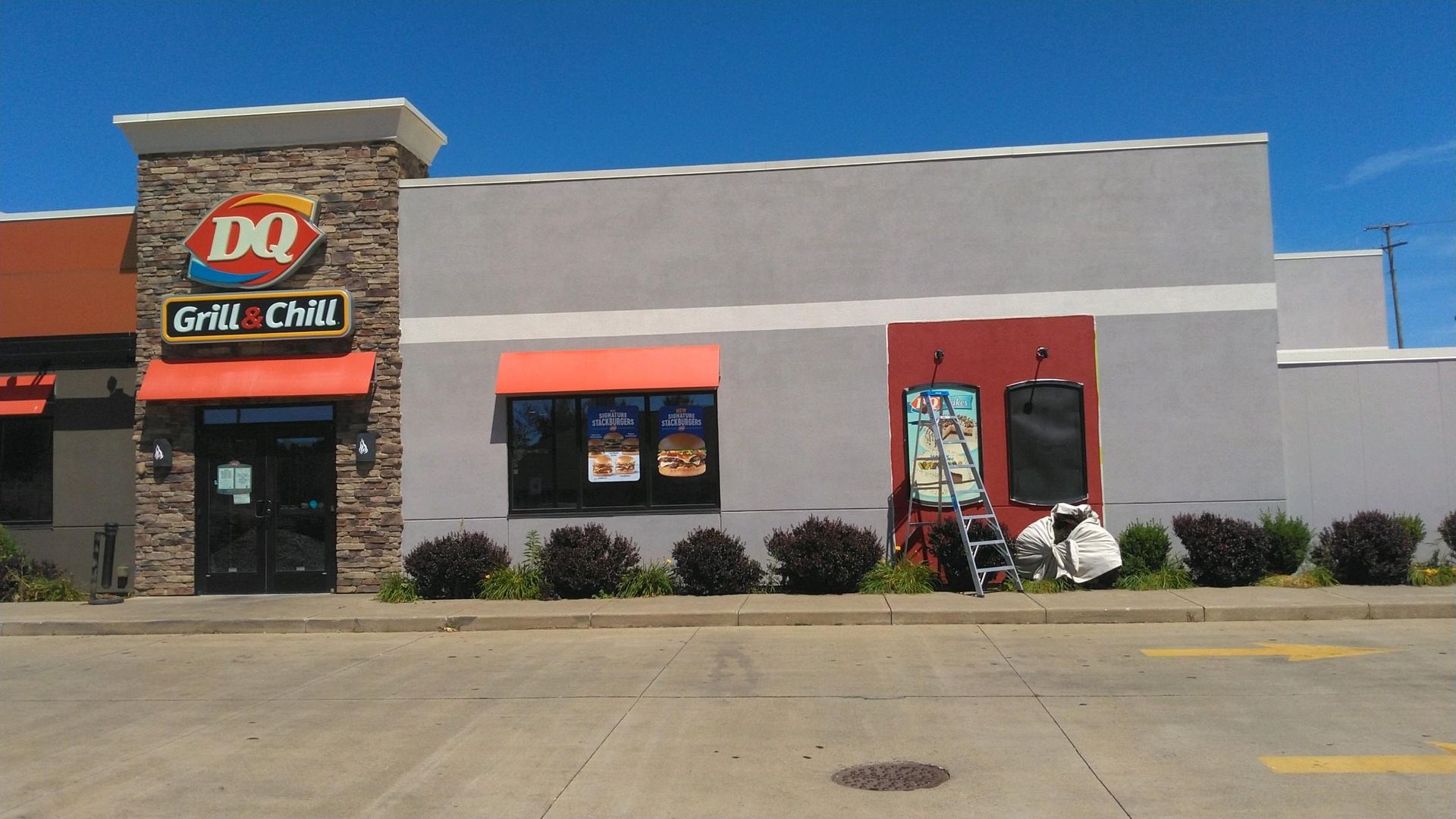 Dairy Queen storefront with stone entry, red awning windows, and parking lot under a clear blue sky