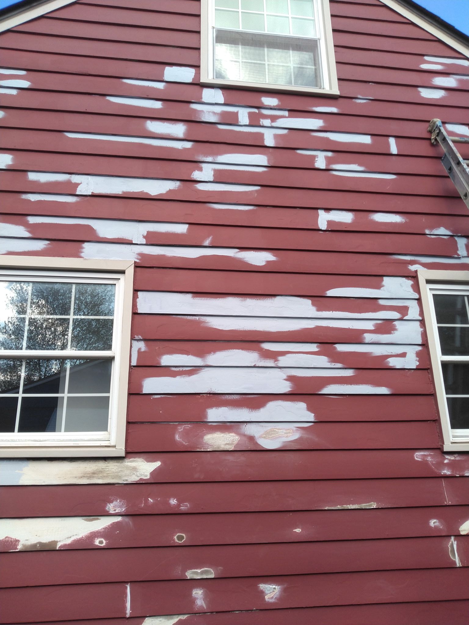 Red house siding with peeling white paint around several windows and trim