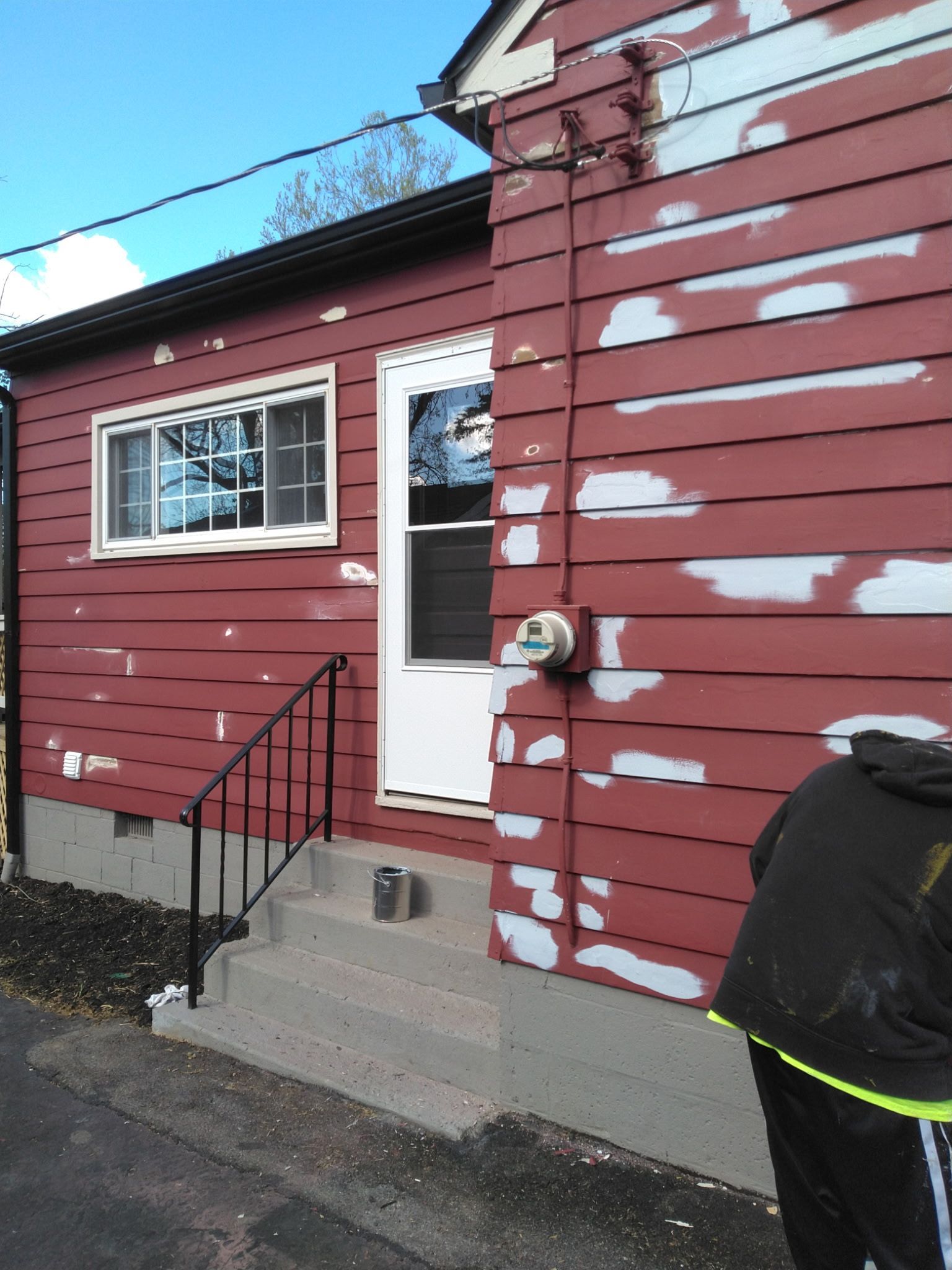 Red house exterior with white trim, front steps, and a partially painted siding wall.