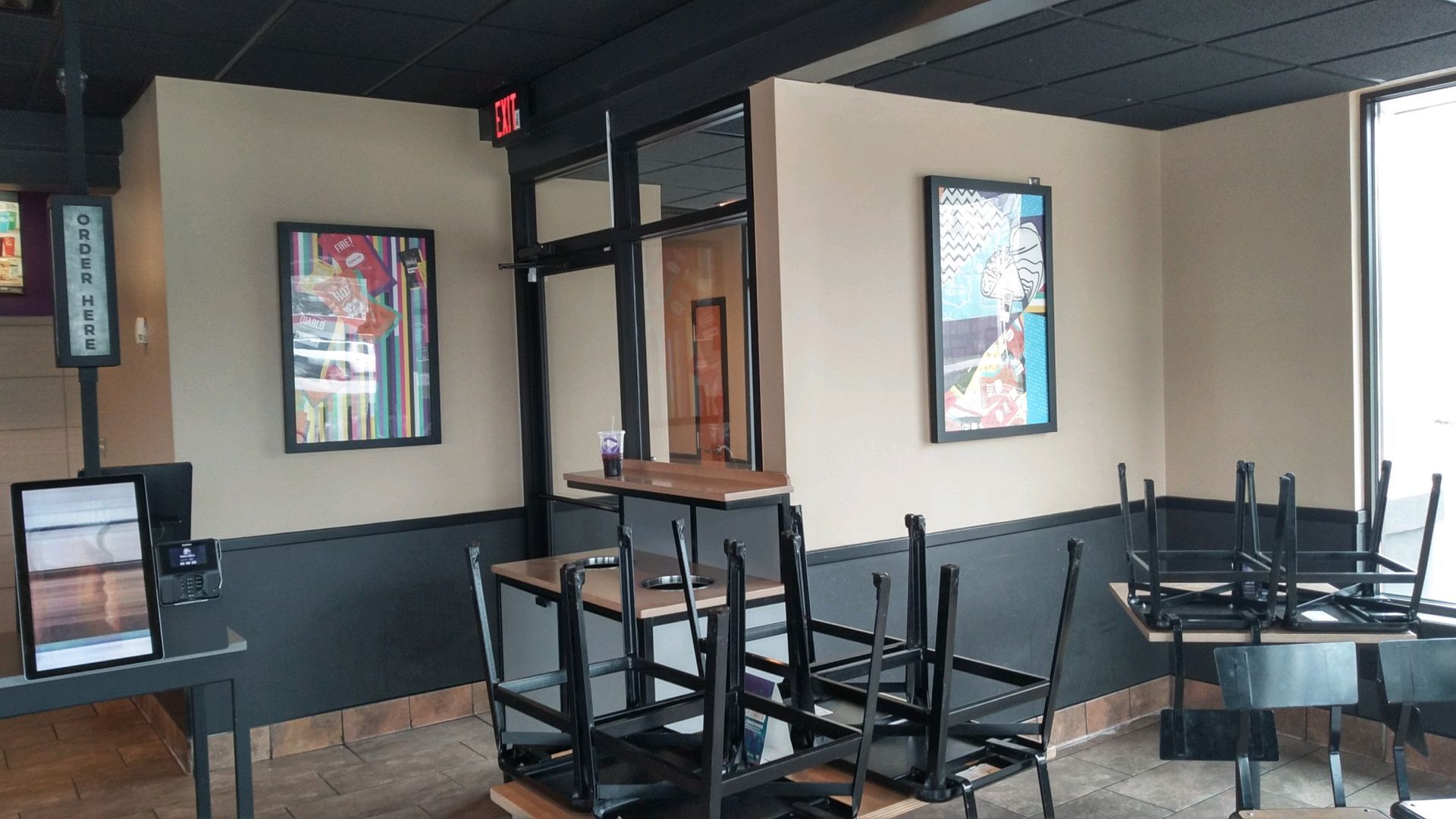Empty restaurant dining area with stacked black chairs, tables, and framed wall art