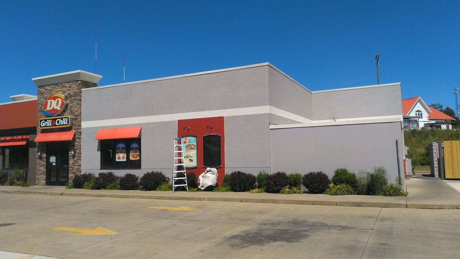 A low-rise restaurant building with red accents and a parking lot under a clear blue sky.