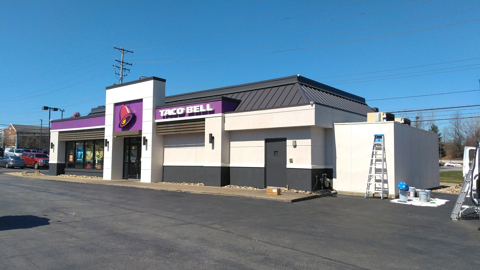 Single-story commercial storefront with purple signage and a ladder outside on a sunny day