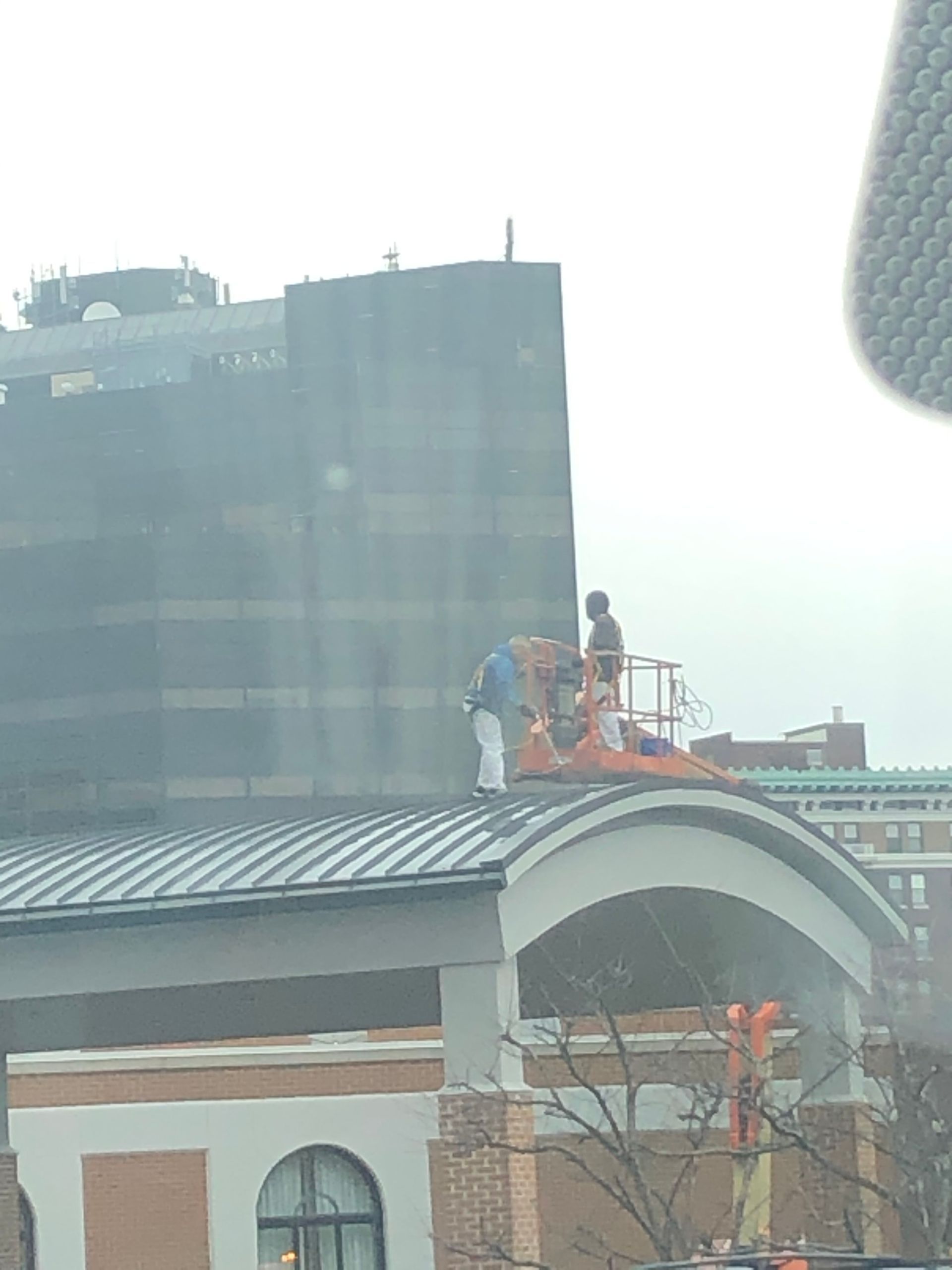Workers on a rooftop beside a white arched structure, with a tall dark building in the background.
