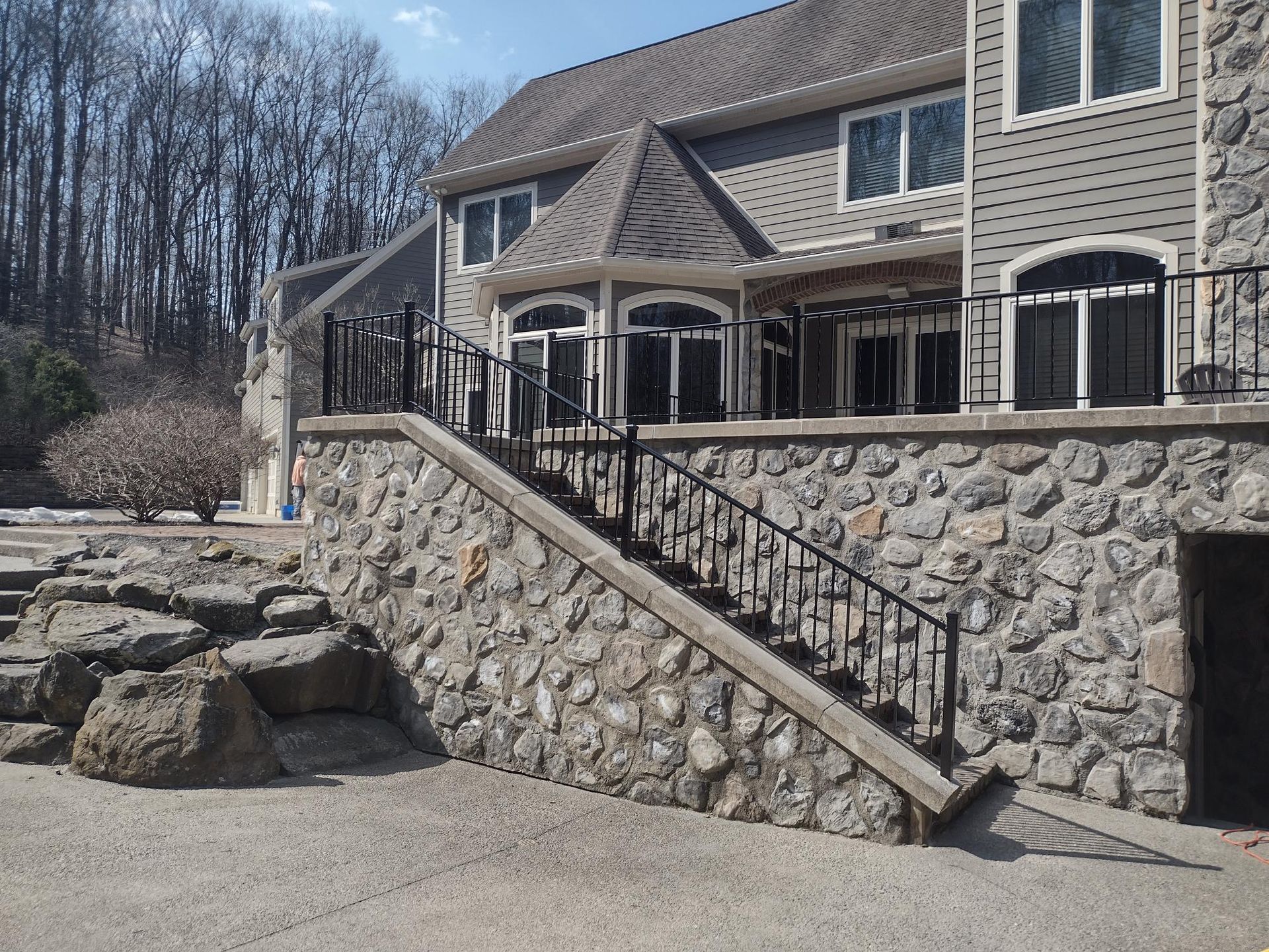 Stone patio and staircase outside a beige house with a wooded backdrop