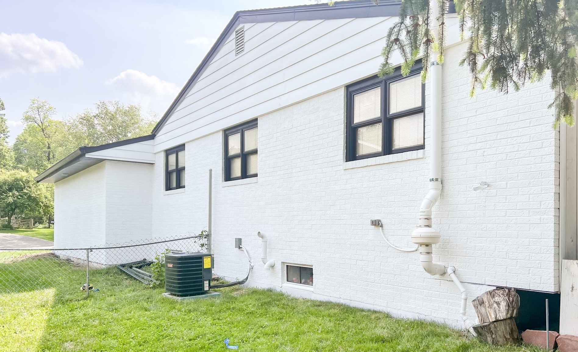 White house side exterior with small windows, grassy yard, and utility fixtures on the wall.