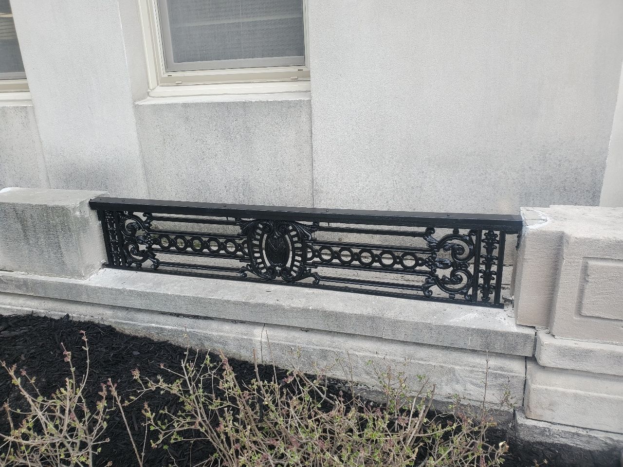 Black ornate metal railing set into a light stone wall below a window.