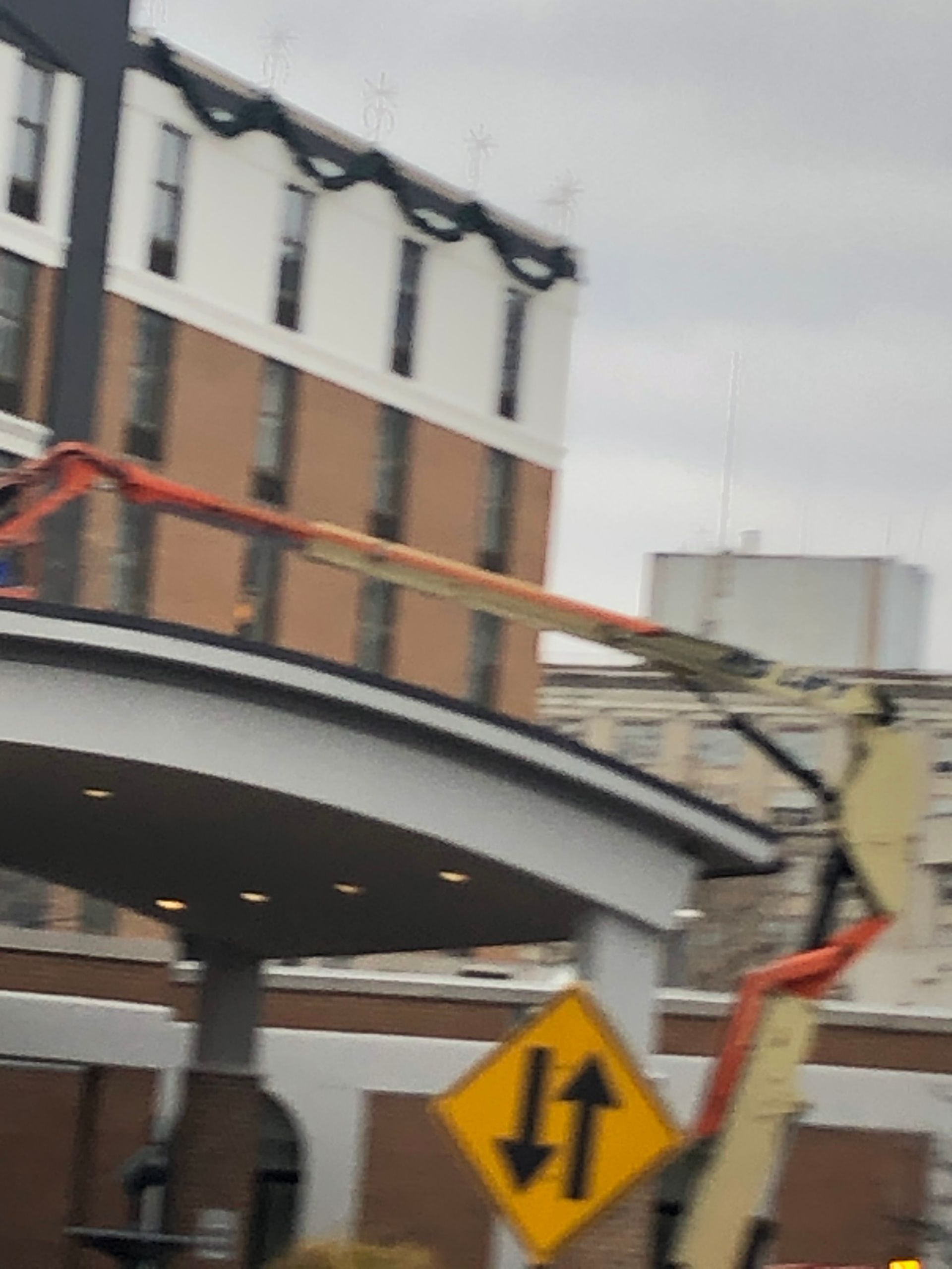 Streetlight maintenance lift beside a building, with a yellow traffic sign in the foreground.