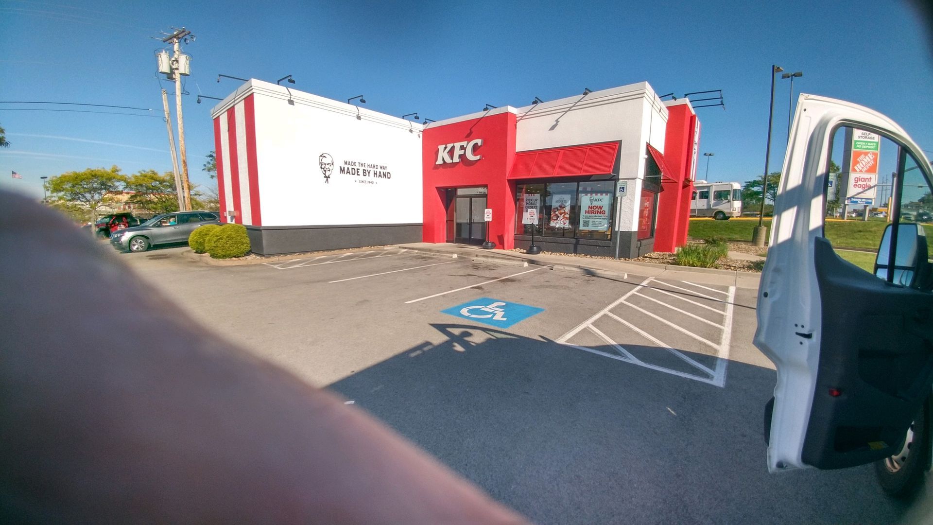 KFC restaurant exterior with red-and-white facade, parking spaces, and an open car door in the foreground