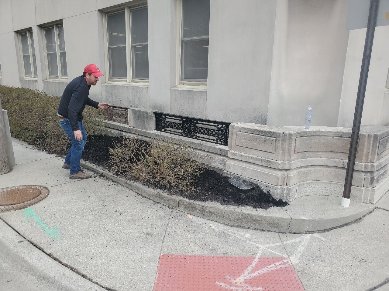 Person inspecting a large dark stain or spill along a building wall on a sidewalk
