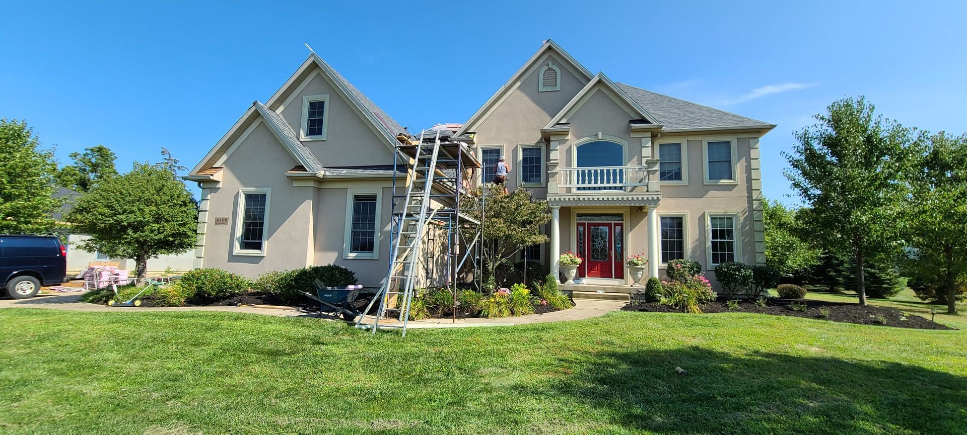 Large gray two-story house with a ladder and scaffolding in the front yard under a blue sky