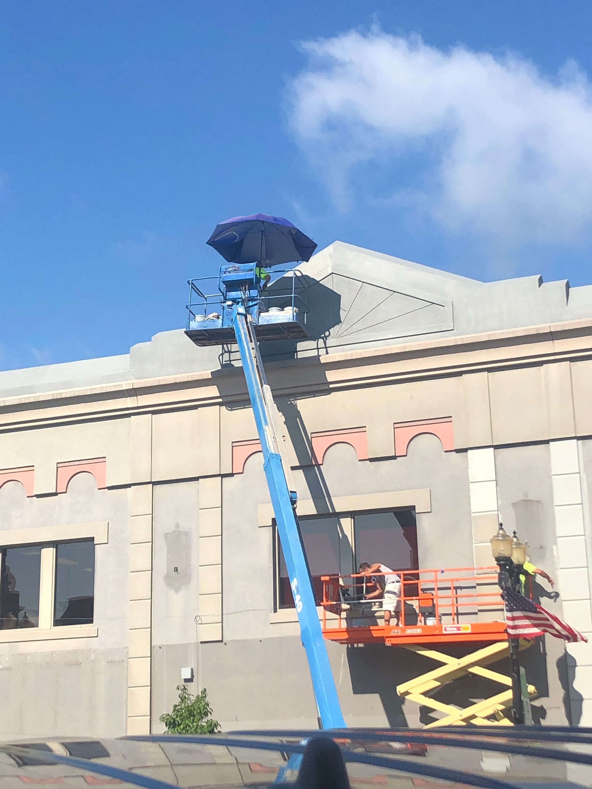 Blue boom lift with workers on a building roof under a clear sky