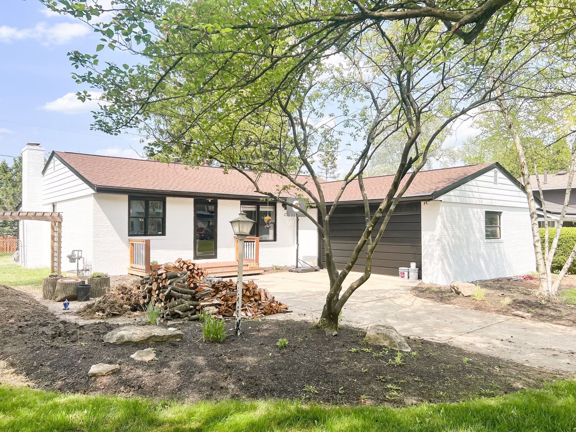 Single-story white house with red roof and porch, front yard trees, and bare landscaping