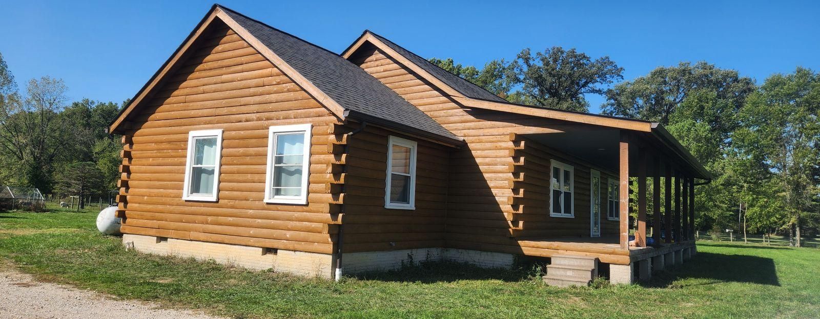 Small log cabin with a dark roof and white-trimmed windows in a grassy rural setting