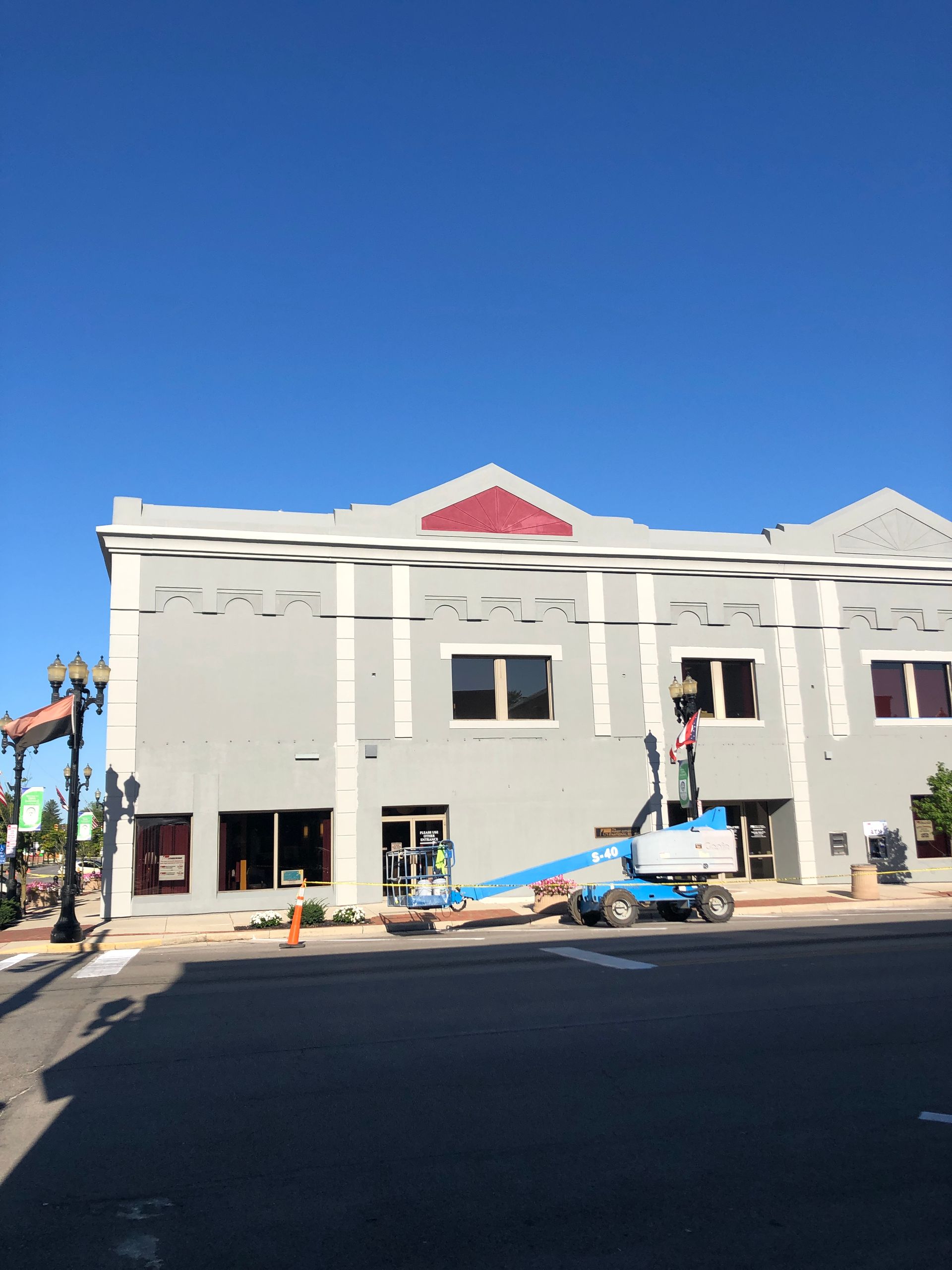 Two-story building under construction with a blue lift and workers outside on a sunny day
