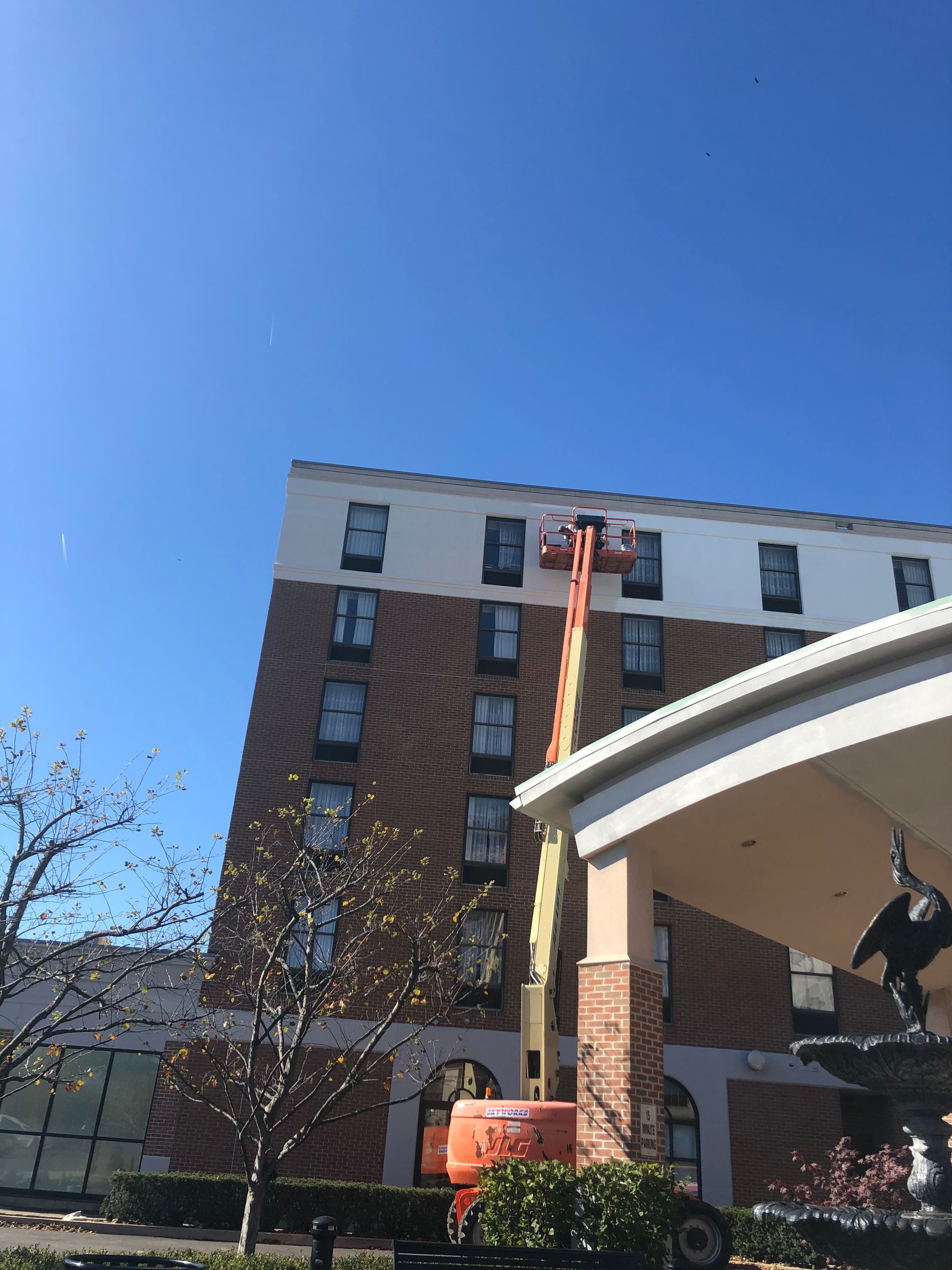 Brick apartment building under a clear blue sky, with a cherry picker lifting a worker near the roofline.