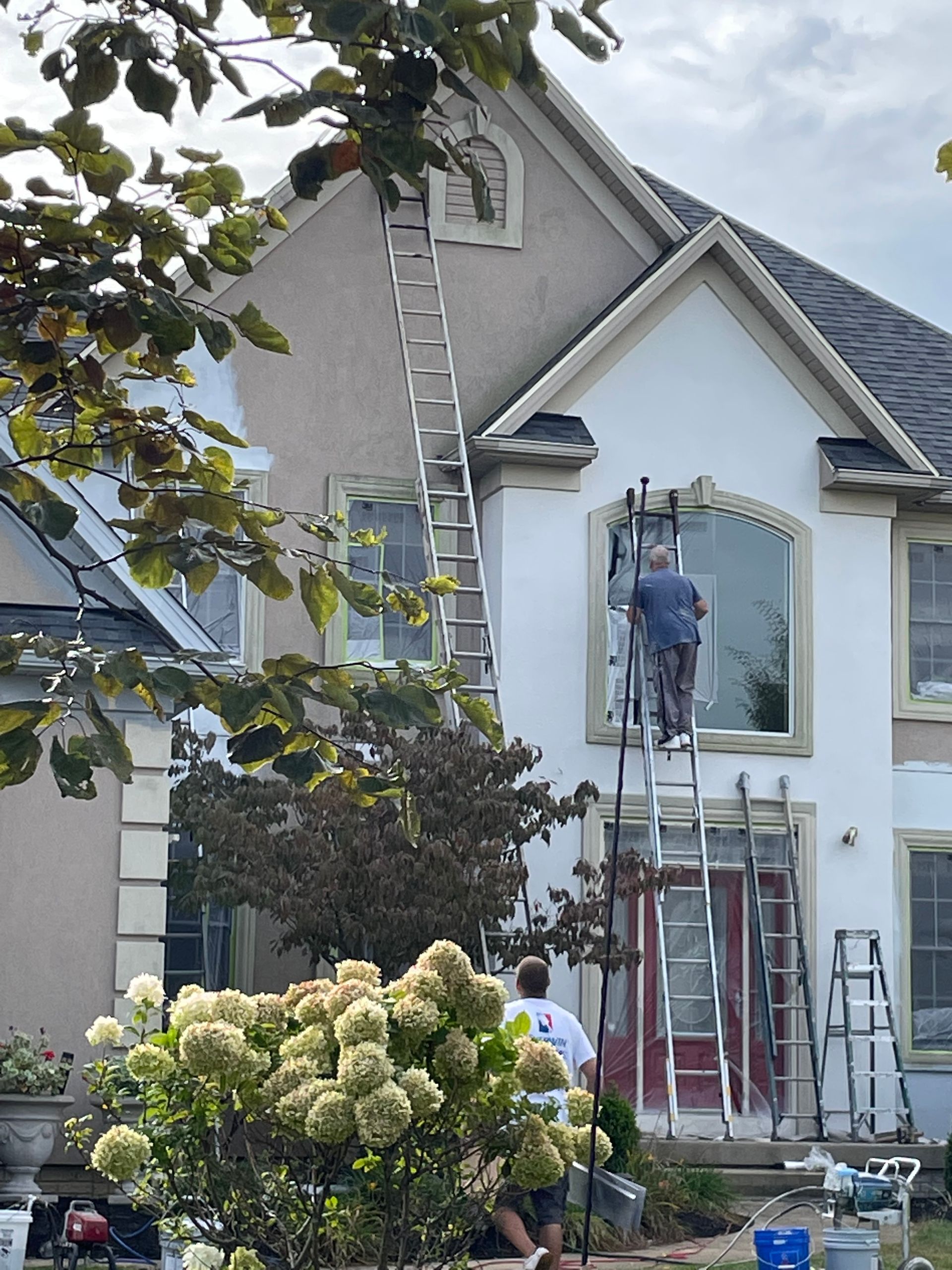 Workers on ladders painting the exterior of a gray house with white trim