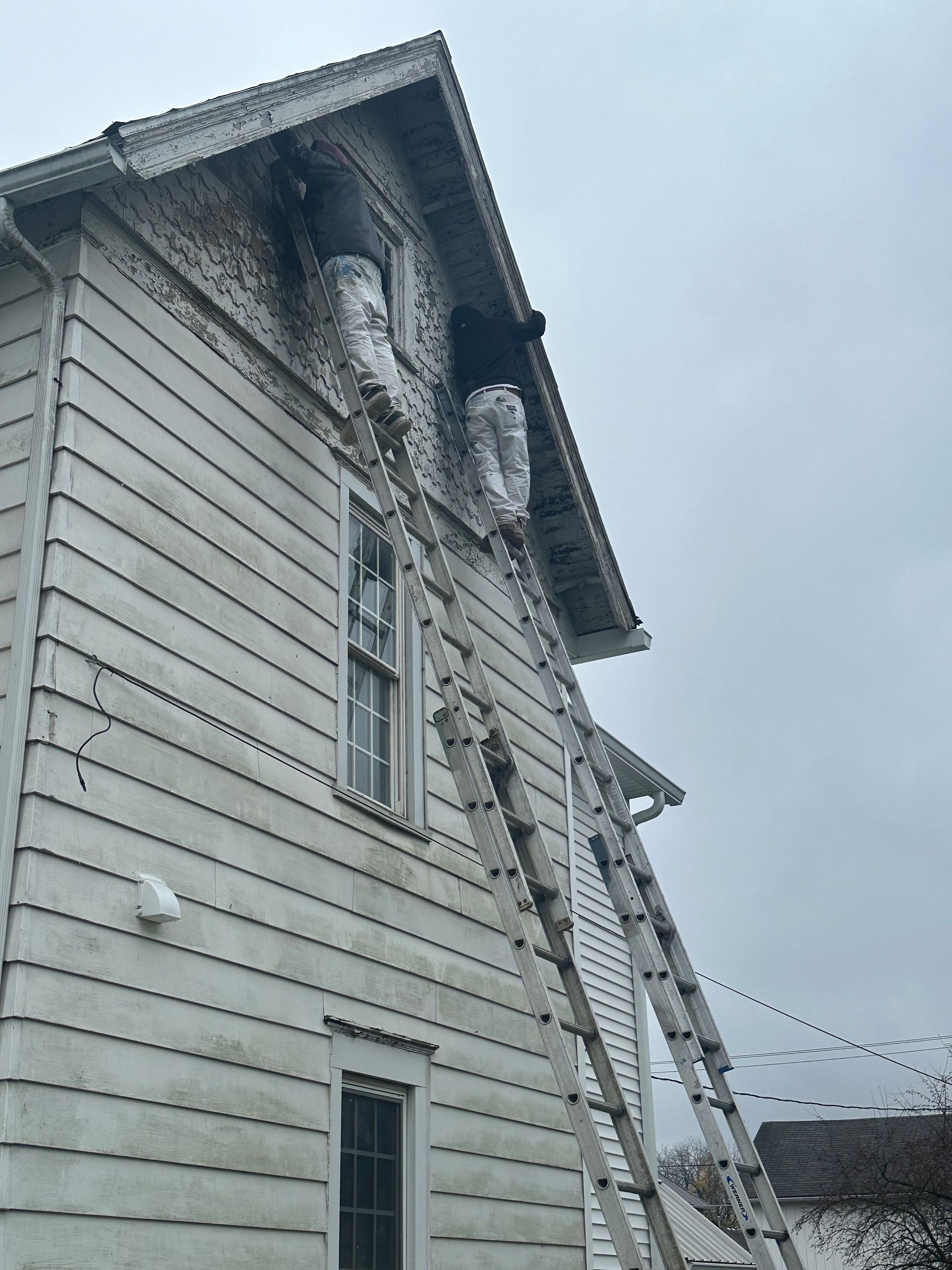 Tall white house with a ladder leaning against the side under a cloudy sky