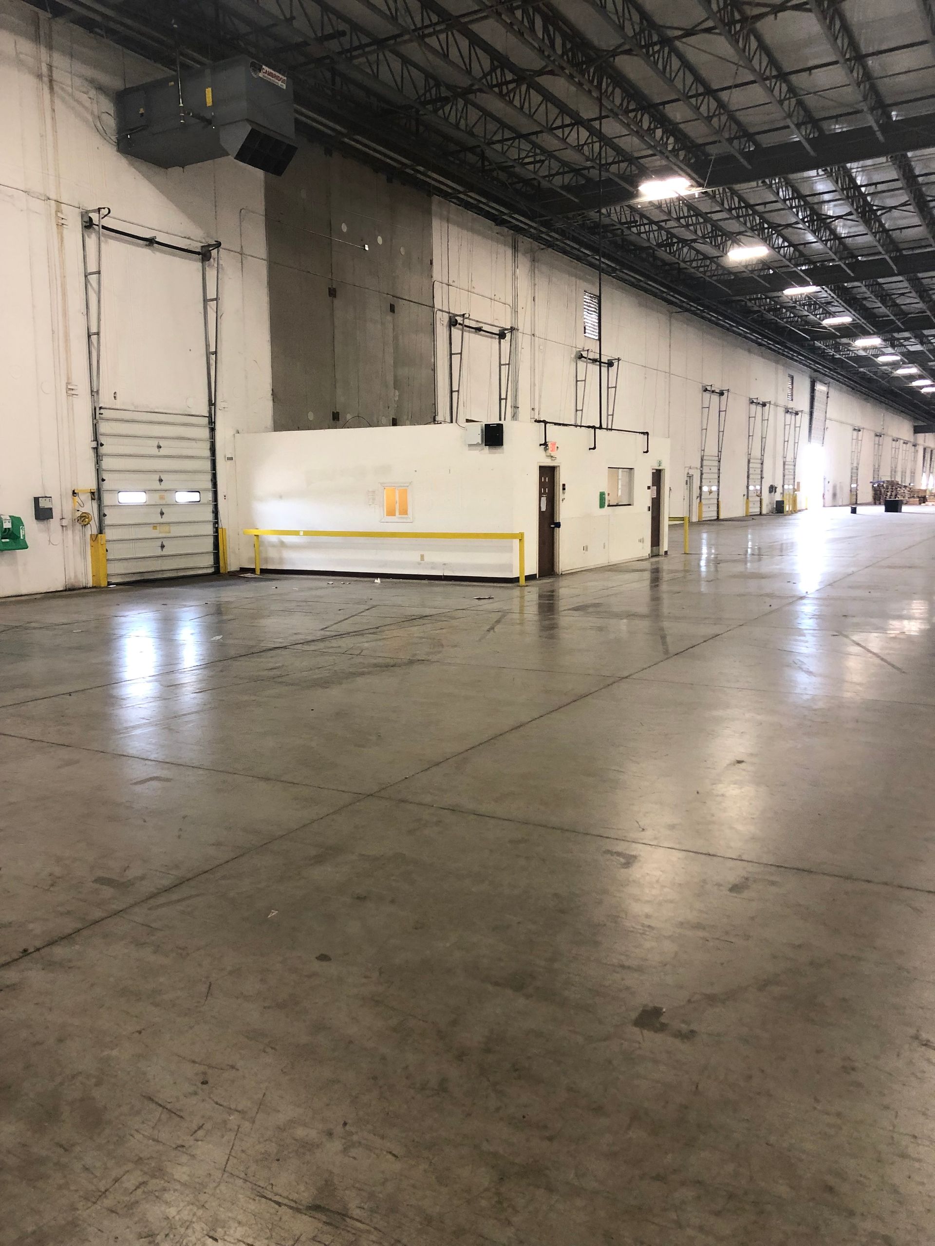 Empty industrial warehouse interior with concrete floor, white walls, and high ceiling lights