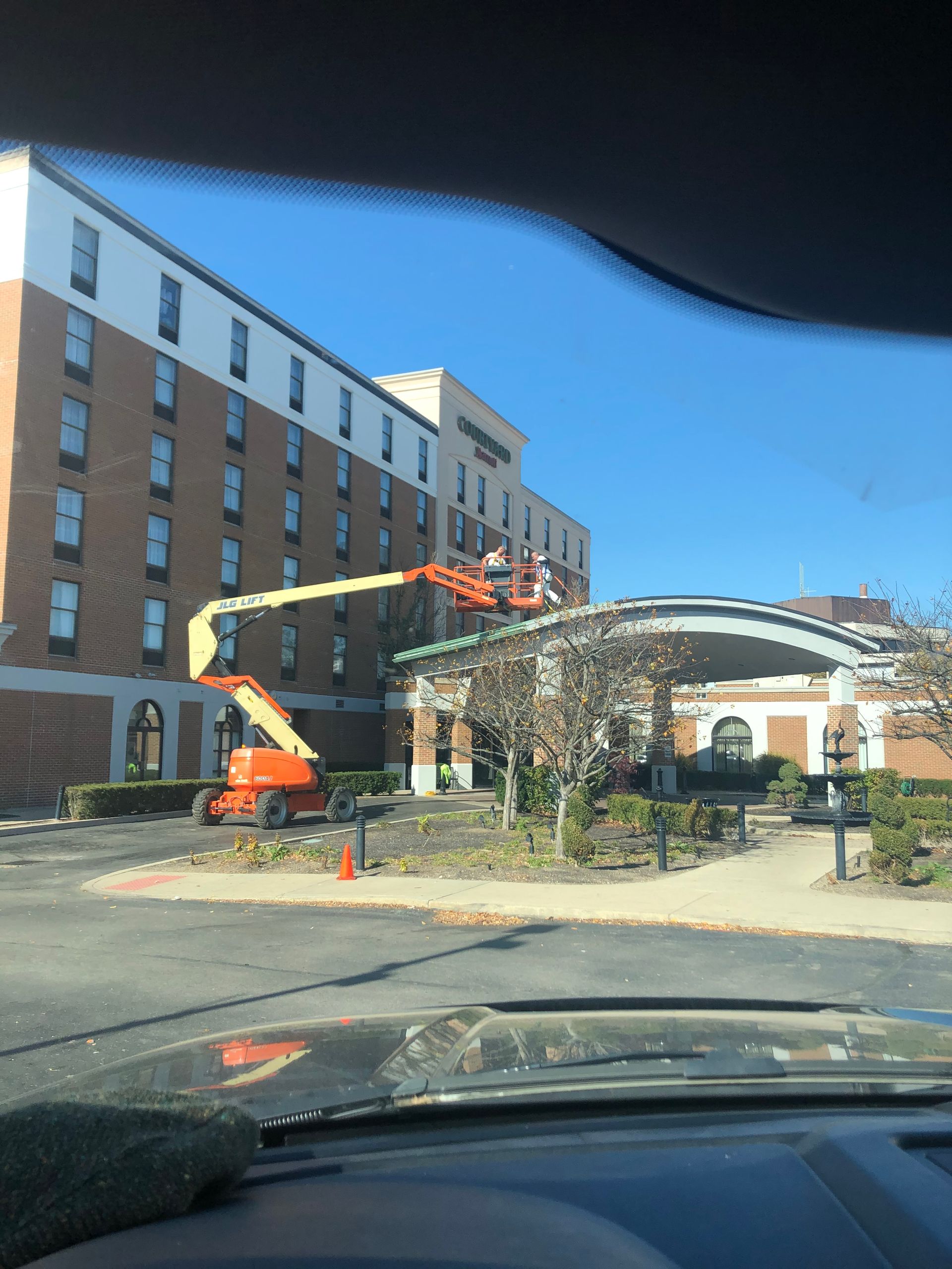 Construction lift beside a brick building under a clear blue sky, viewed from inside a car.