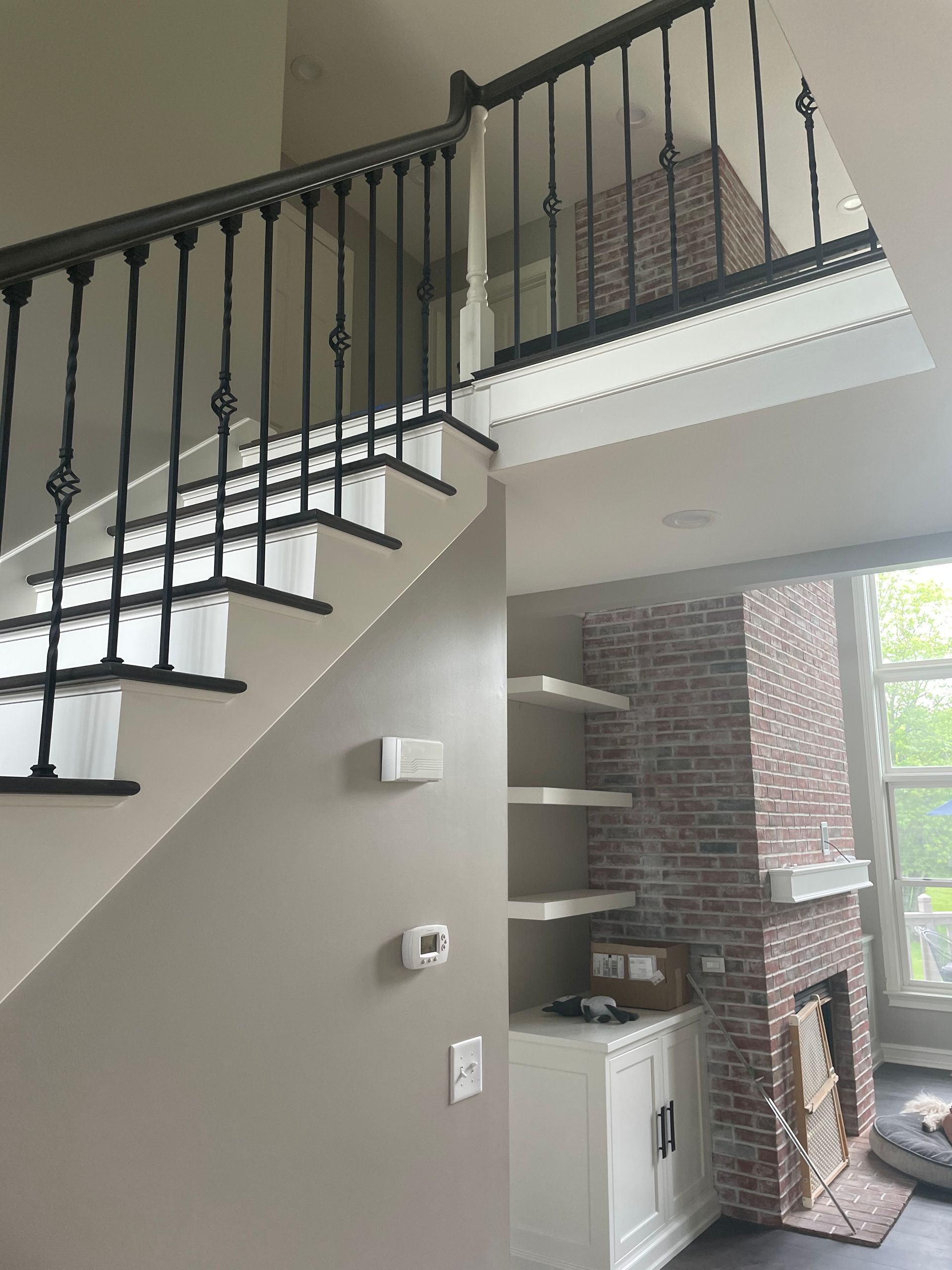 Interior staircase with black railings, white steps, and built-in shelves beside a brick fireplace.