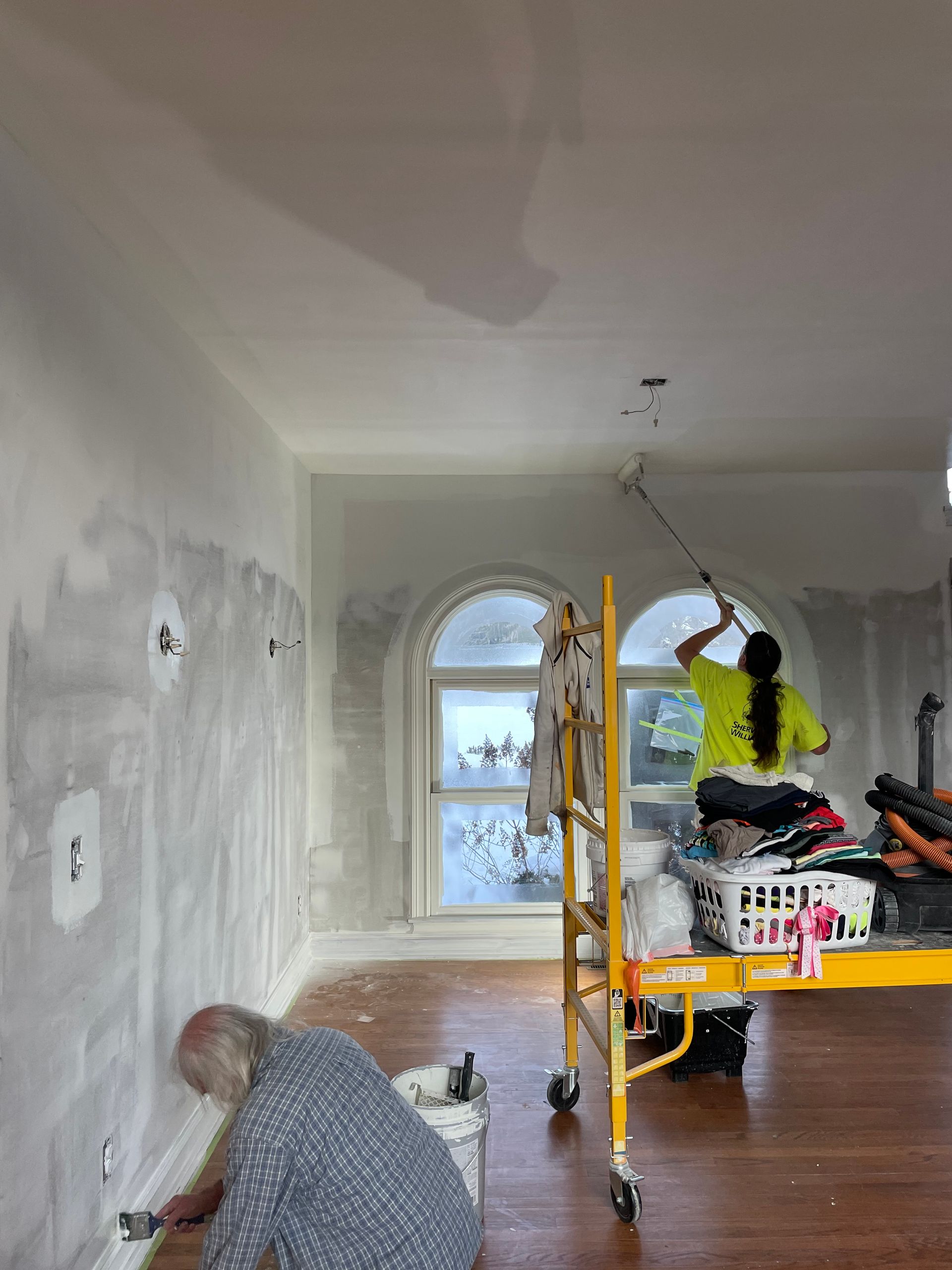 Person kneeling in a room under renovation, with drywall dust and a scaffold near an arched window.