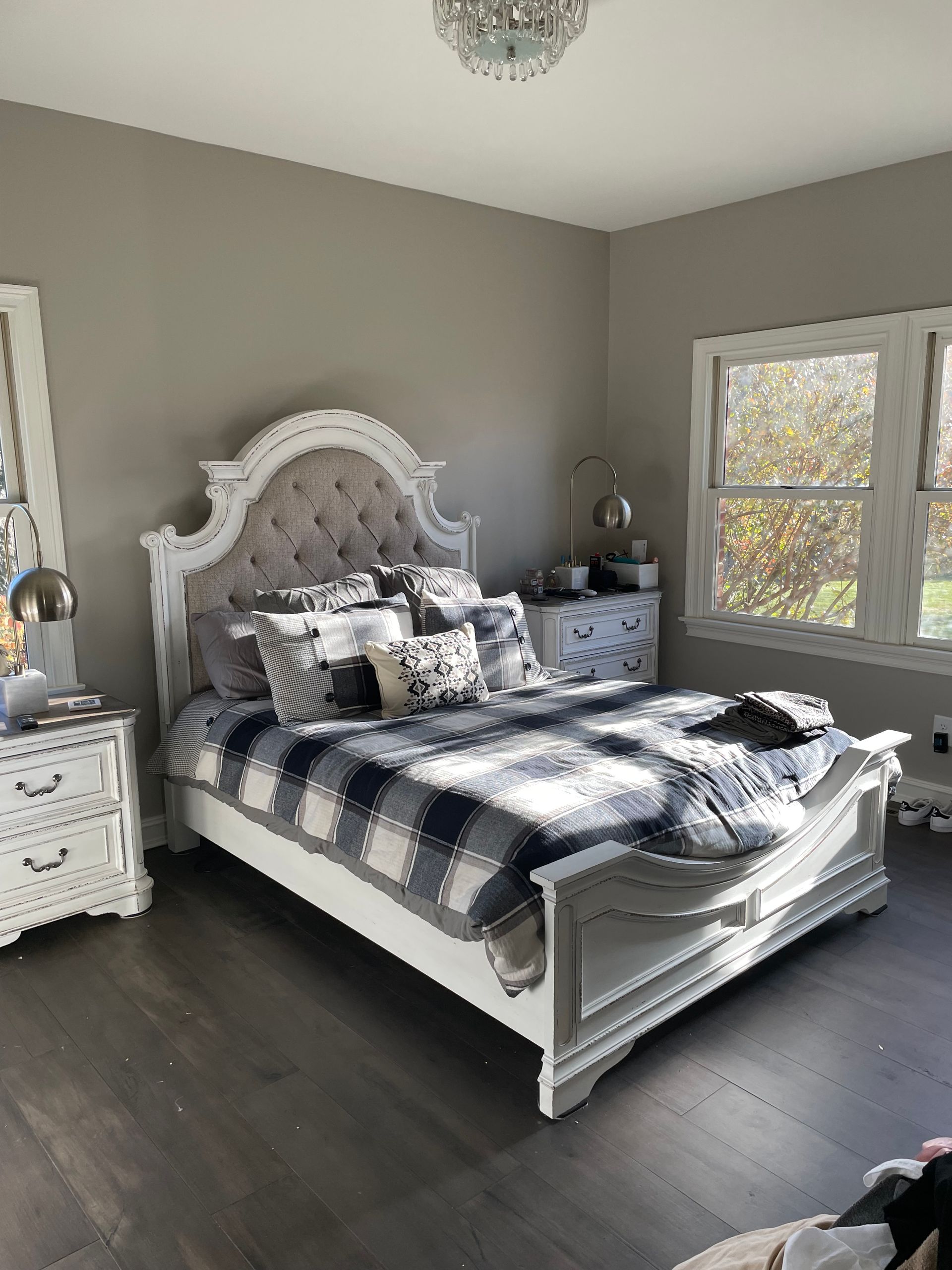 Elegant bedroom with a white tufted bed, gray walls, dark floor, and matching nightstands by a window.