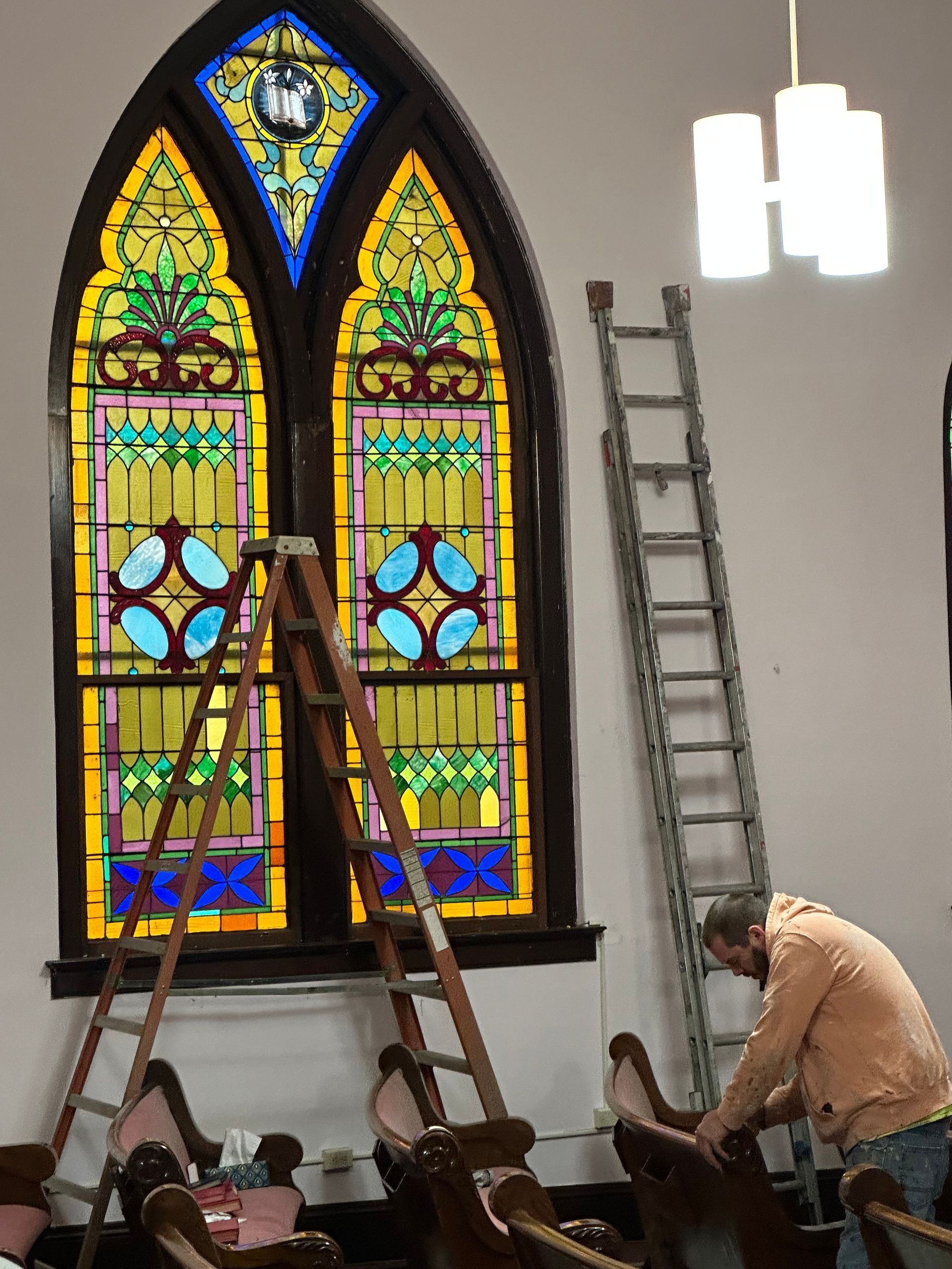 Workers installing stained glass window panels in a church interior, with ladders and scaffolding.