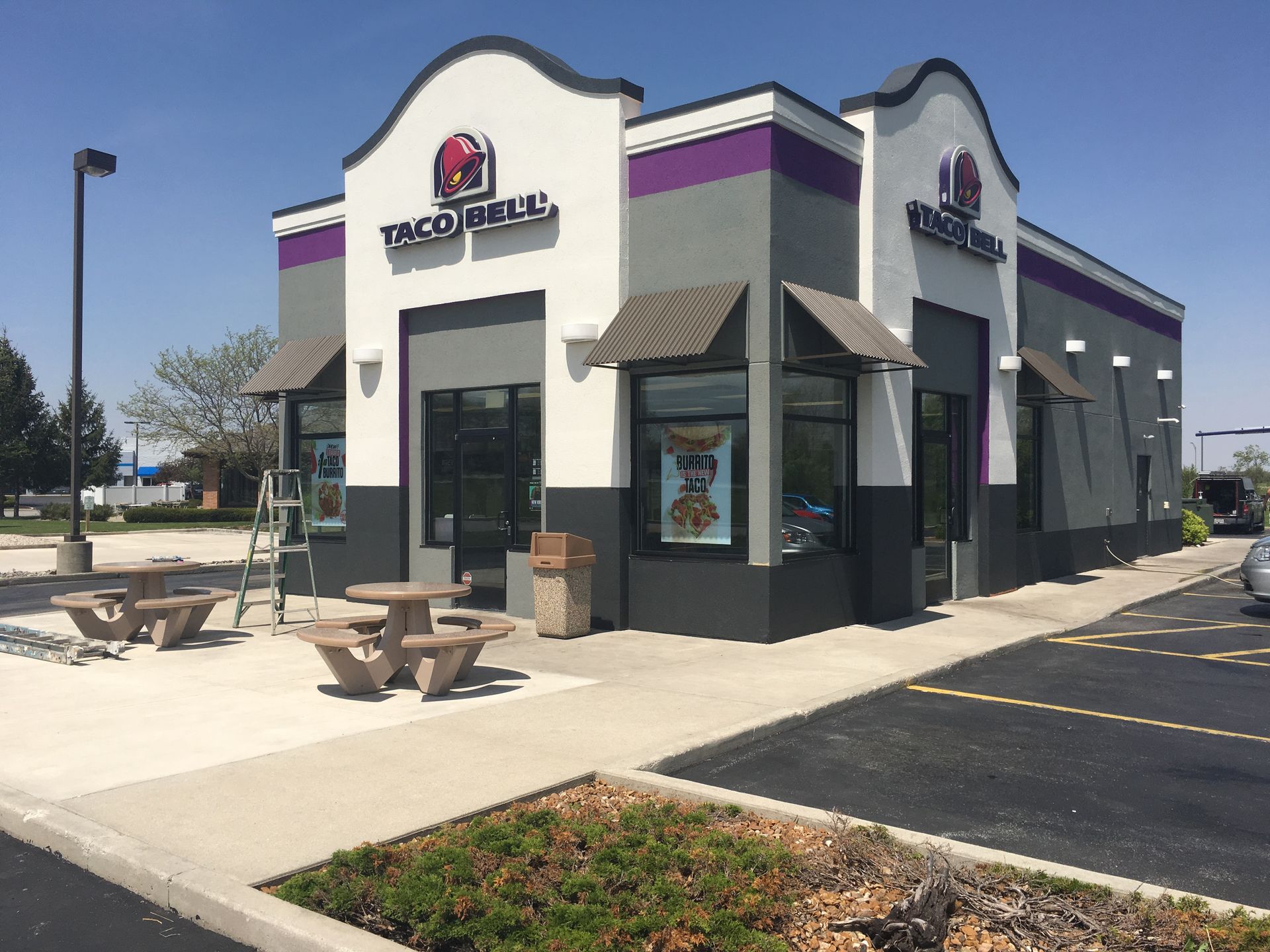 Taco Bell restaurant exterior with outdoor tables and parking lot on a sunny day