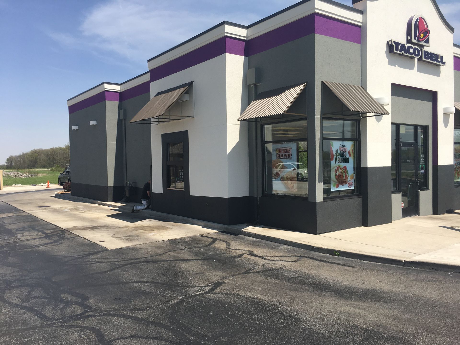 Corner view of a Taco Bell restaurant with white walls, purple trim, and black awnings beside an empty parking lot