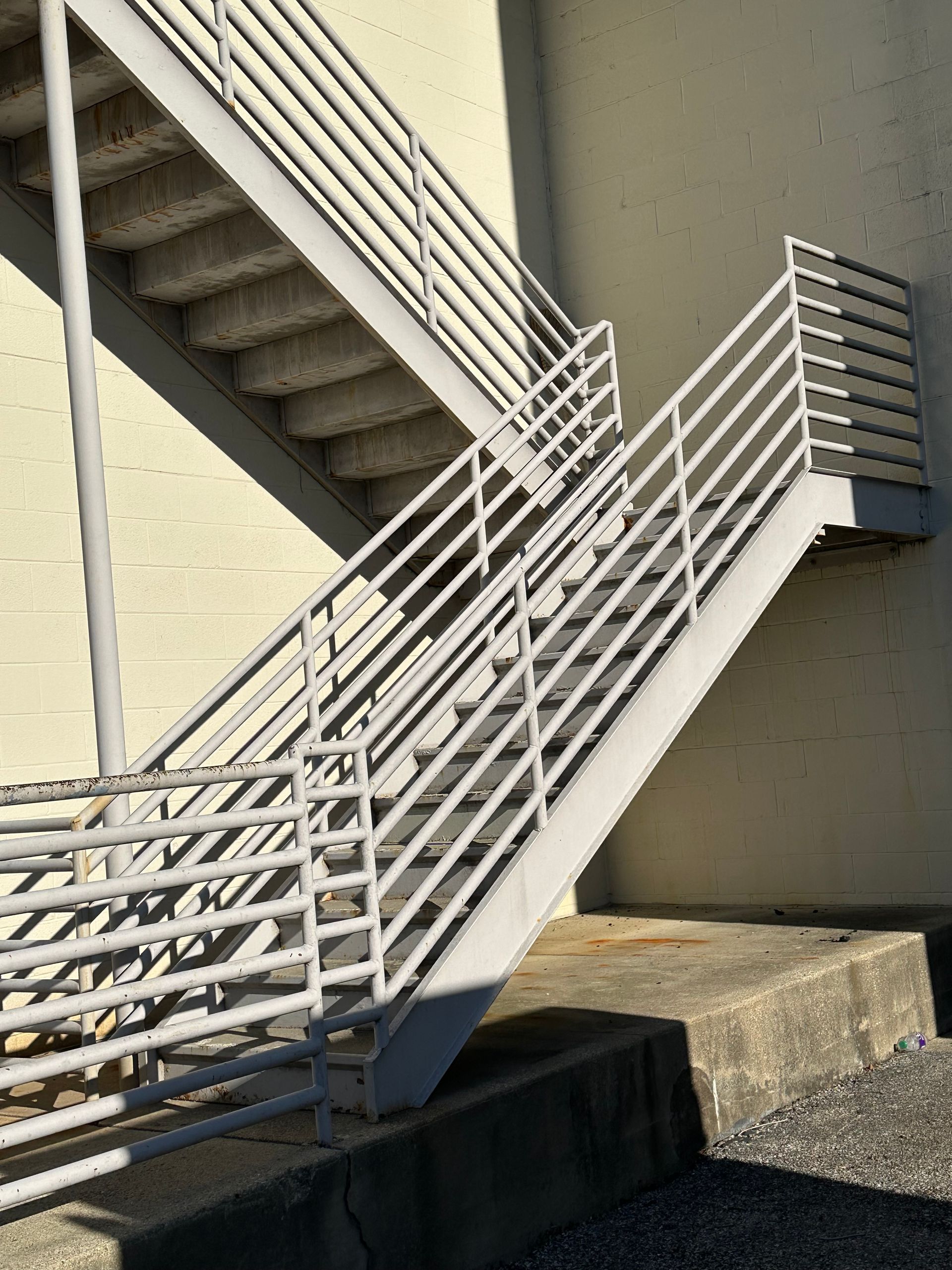 Outdoor metal stairway with white railings beside a beige building, lit by sunlight.