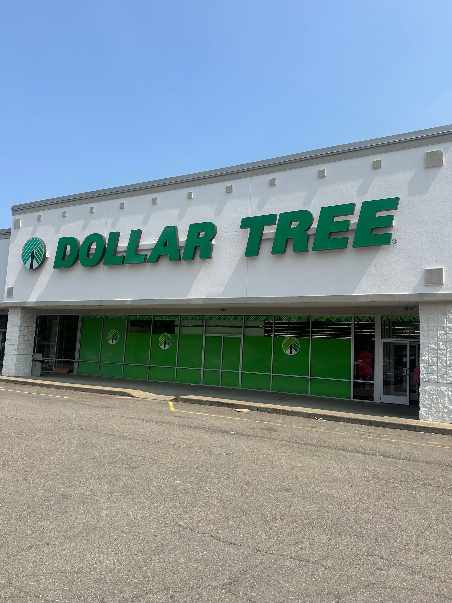 Dollar Tree storefront with green sign and doors in a strip mall parking lot under a clear blue sky