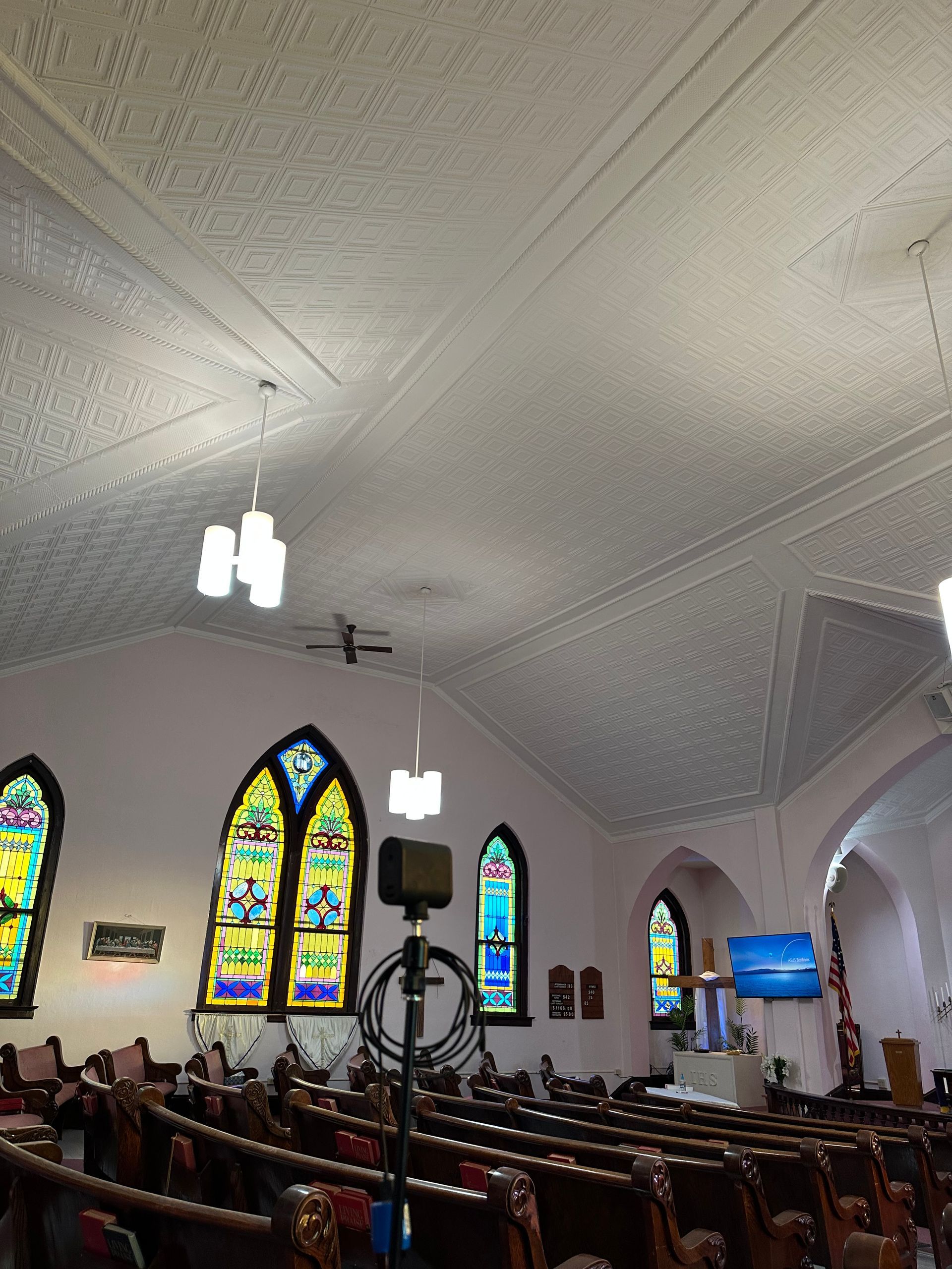Church sanctuary with stained-glass windows, wooden pews, and a chandelier-lit ceiling