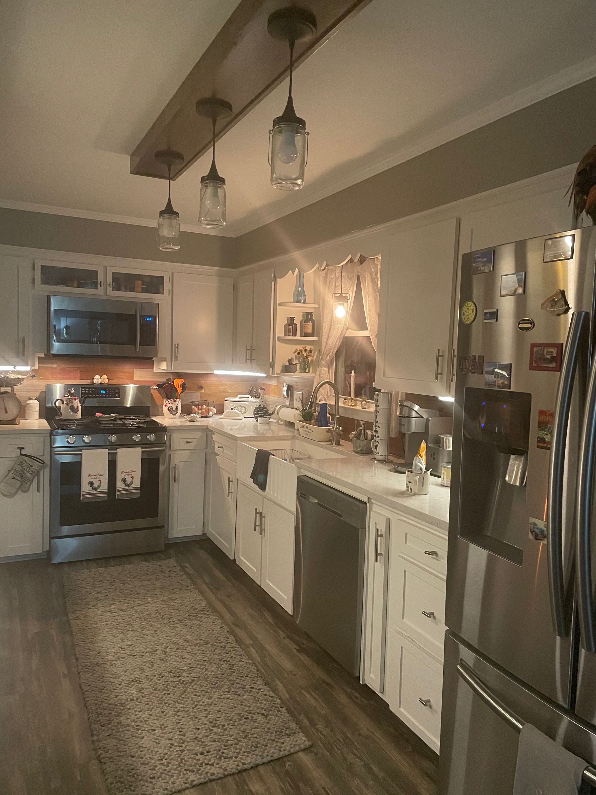 Warm, narrow kitchen with white cabinets, stainless appliances, pendant lights, and a patterned runner rug.