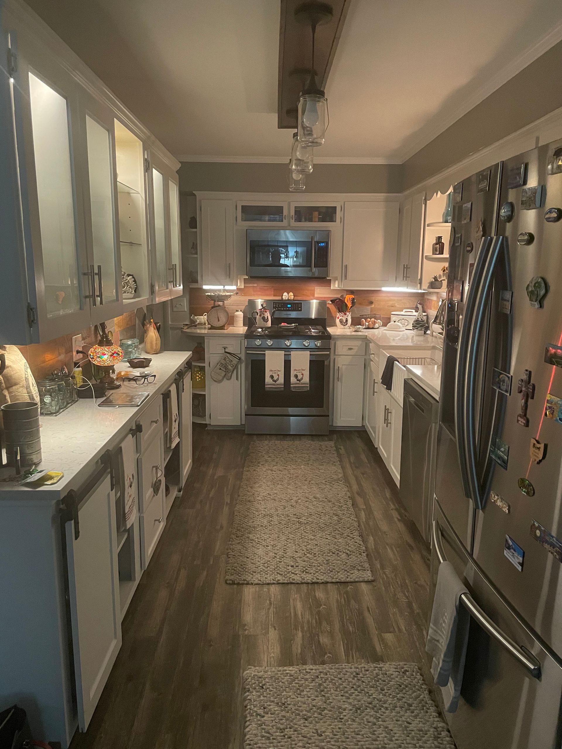 Narrow galley kitchen with white cabinets, stainless appliances, and a patterned runner rug.