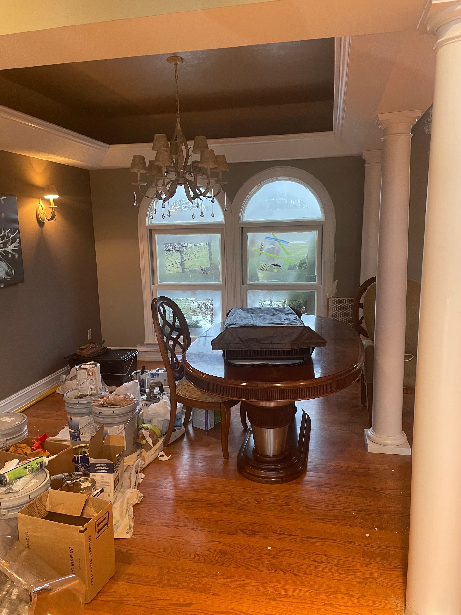 Elegant dining room with round wooden table, chandelier, and arched window overlooking greenery