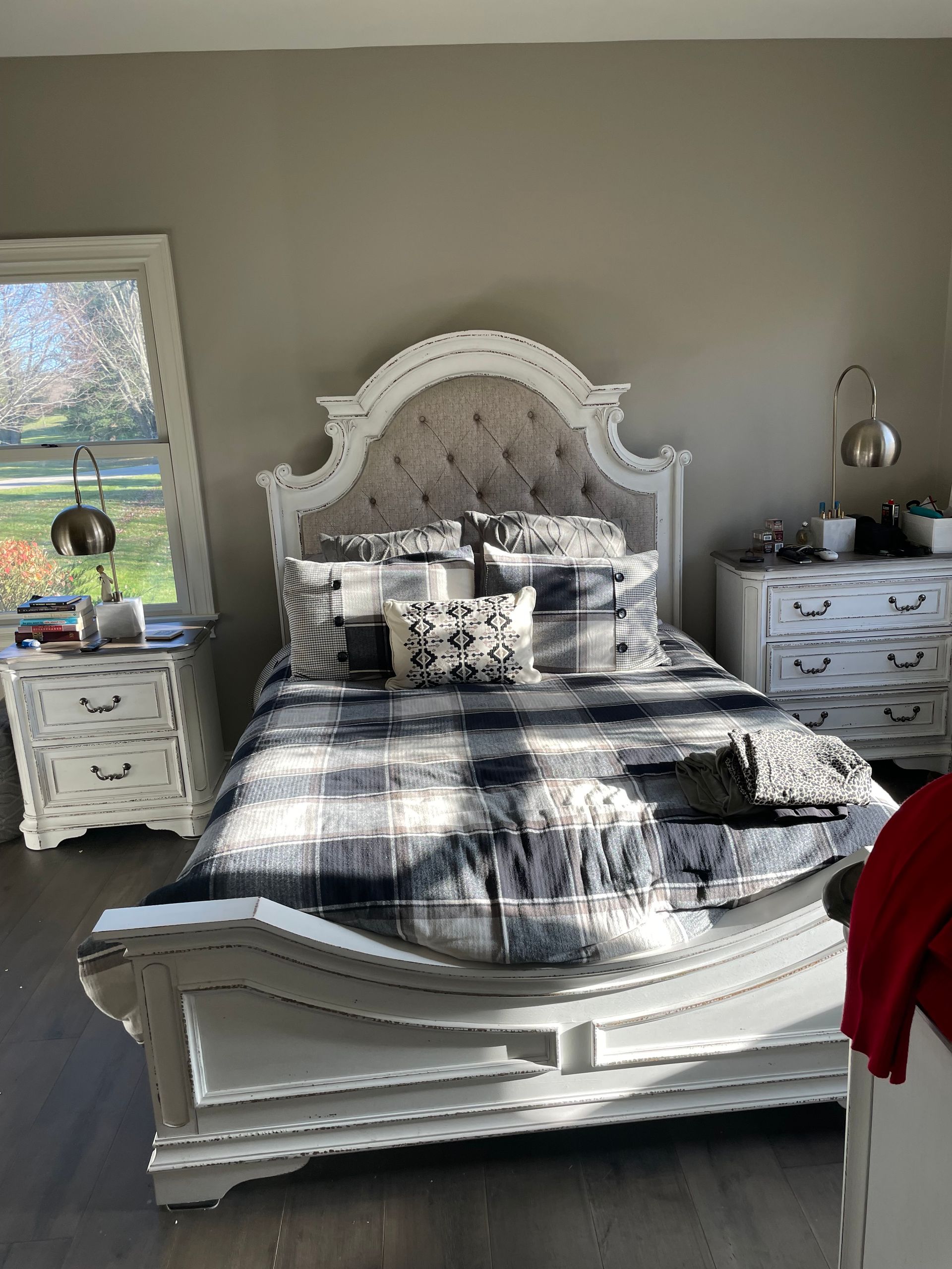 White ornate bed with patterned bedding in a bright bedroom, flanked by matching nightstands and lamps.