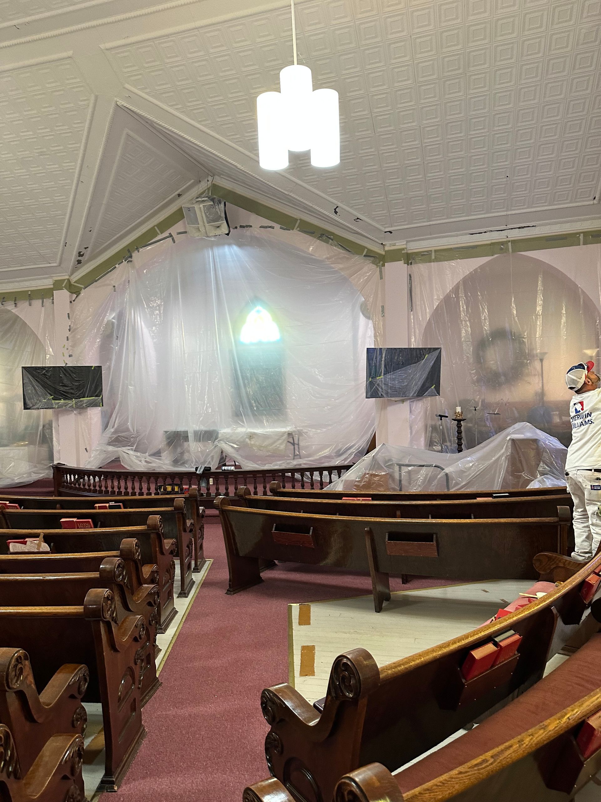 Interior of a church under renovation, with pews, a covered altar, and draped plastic along the front.