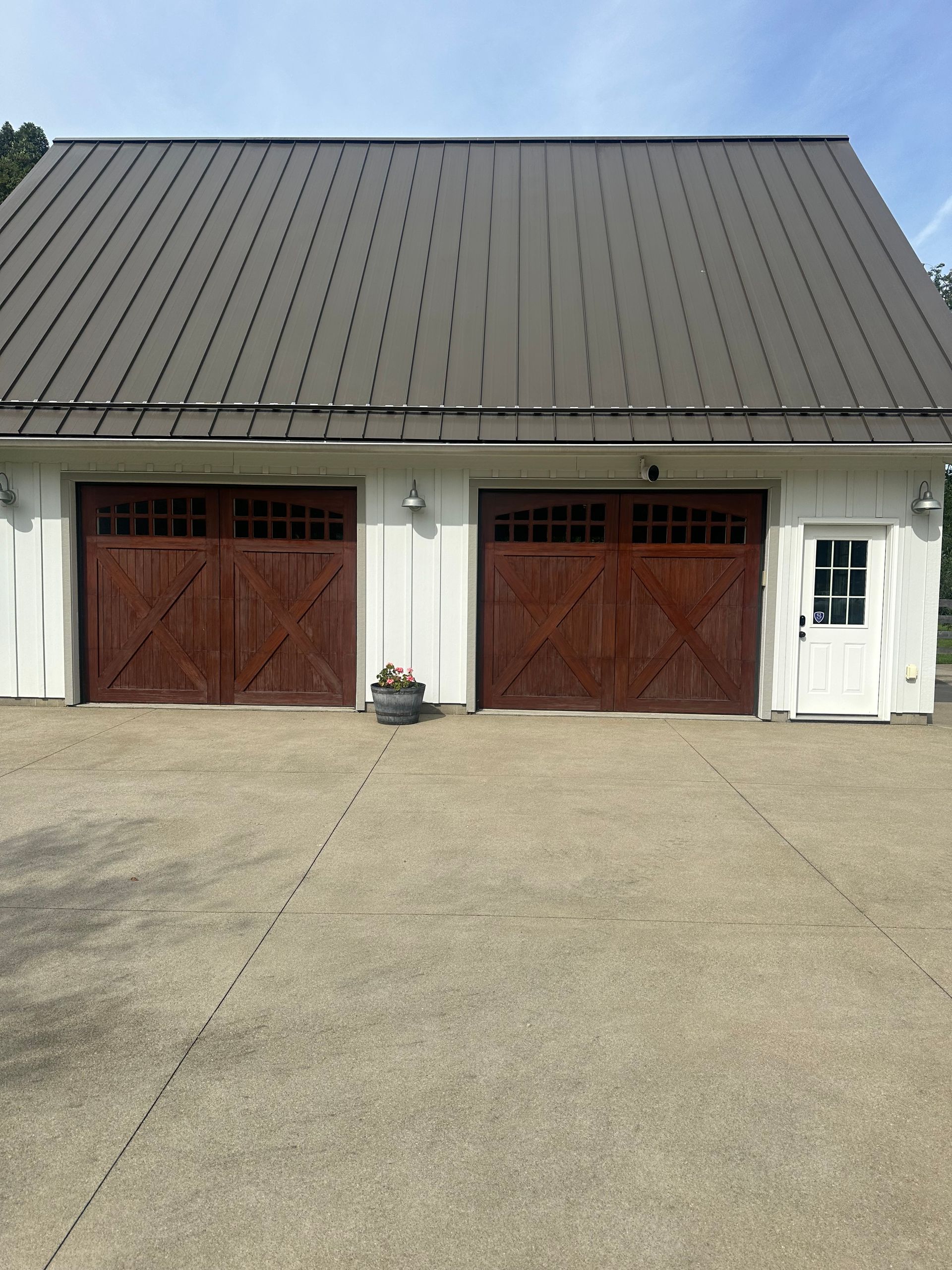 White building with a gray metal roof and two brown garage doors on a concrete driveway