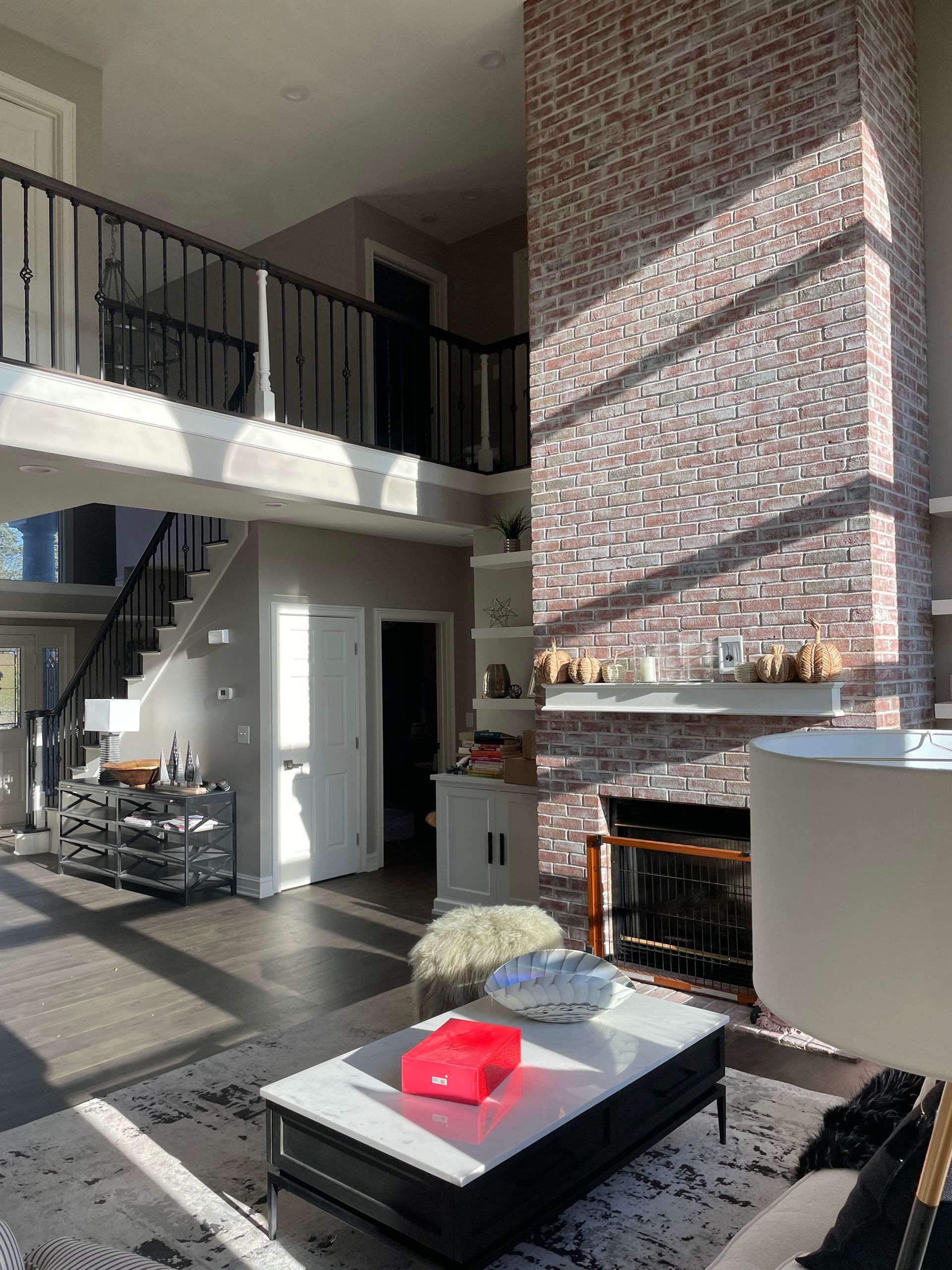 Modern living room with staircase, brick fireplace, and coffee table in sunlight