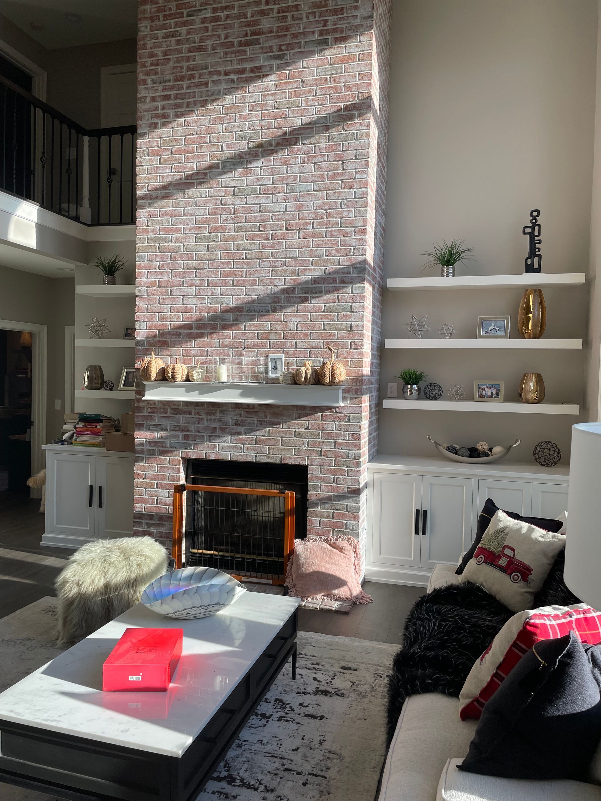 Bright living room with tall brick fireplace, white shelves, and black-and-white furniture with red accents.