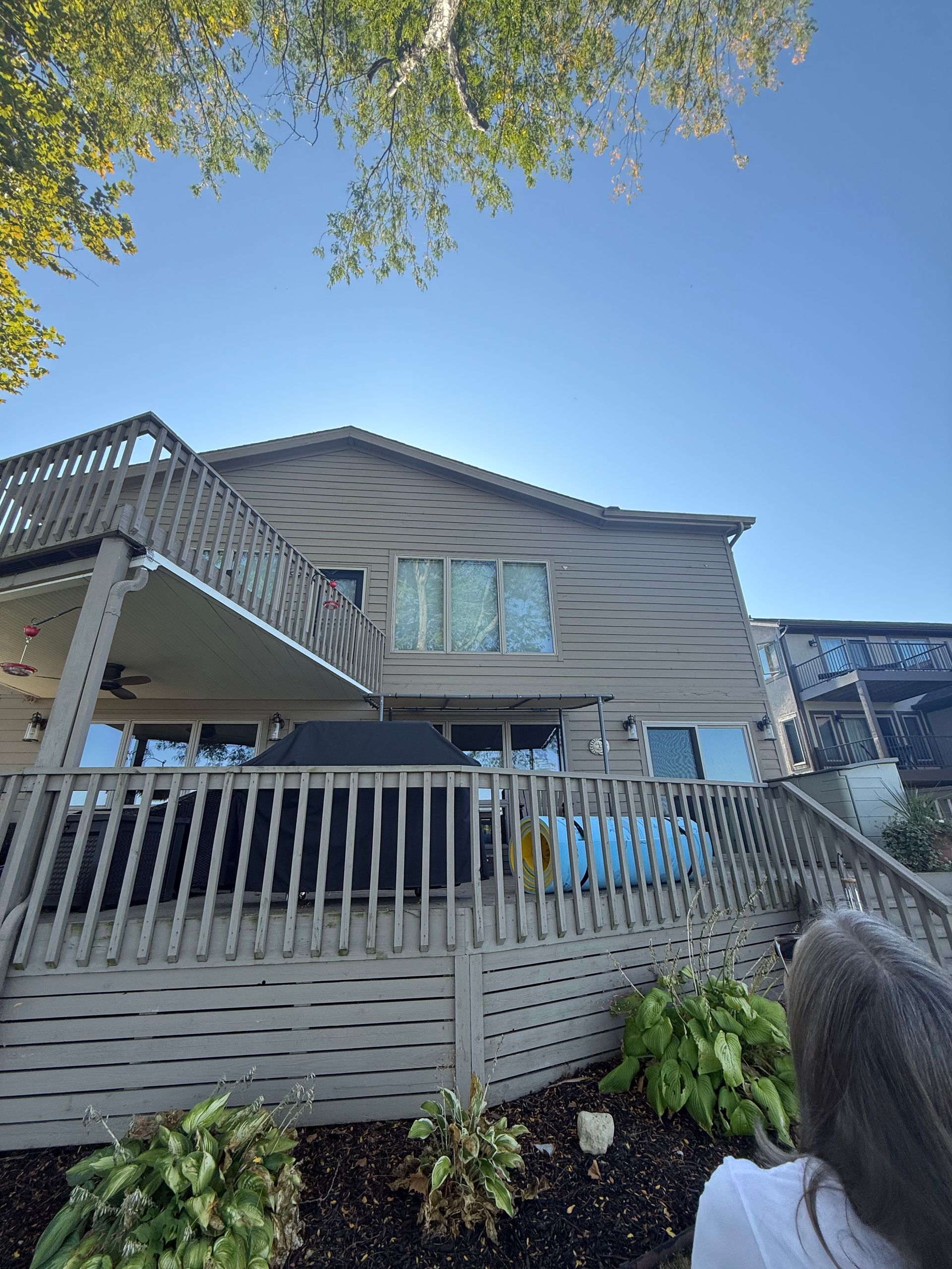 House exterior with gray siding, white fence, and a bright blue sky above flowering shrubs