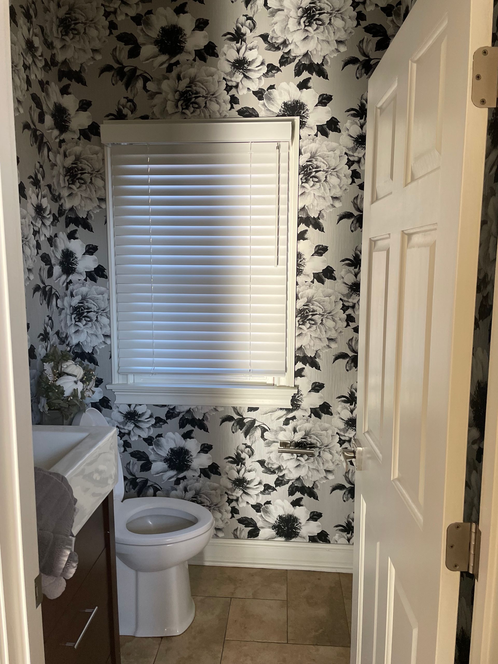 Small bathroom with floral wallpaper, window blinds, toilet, and vanity sink.