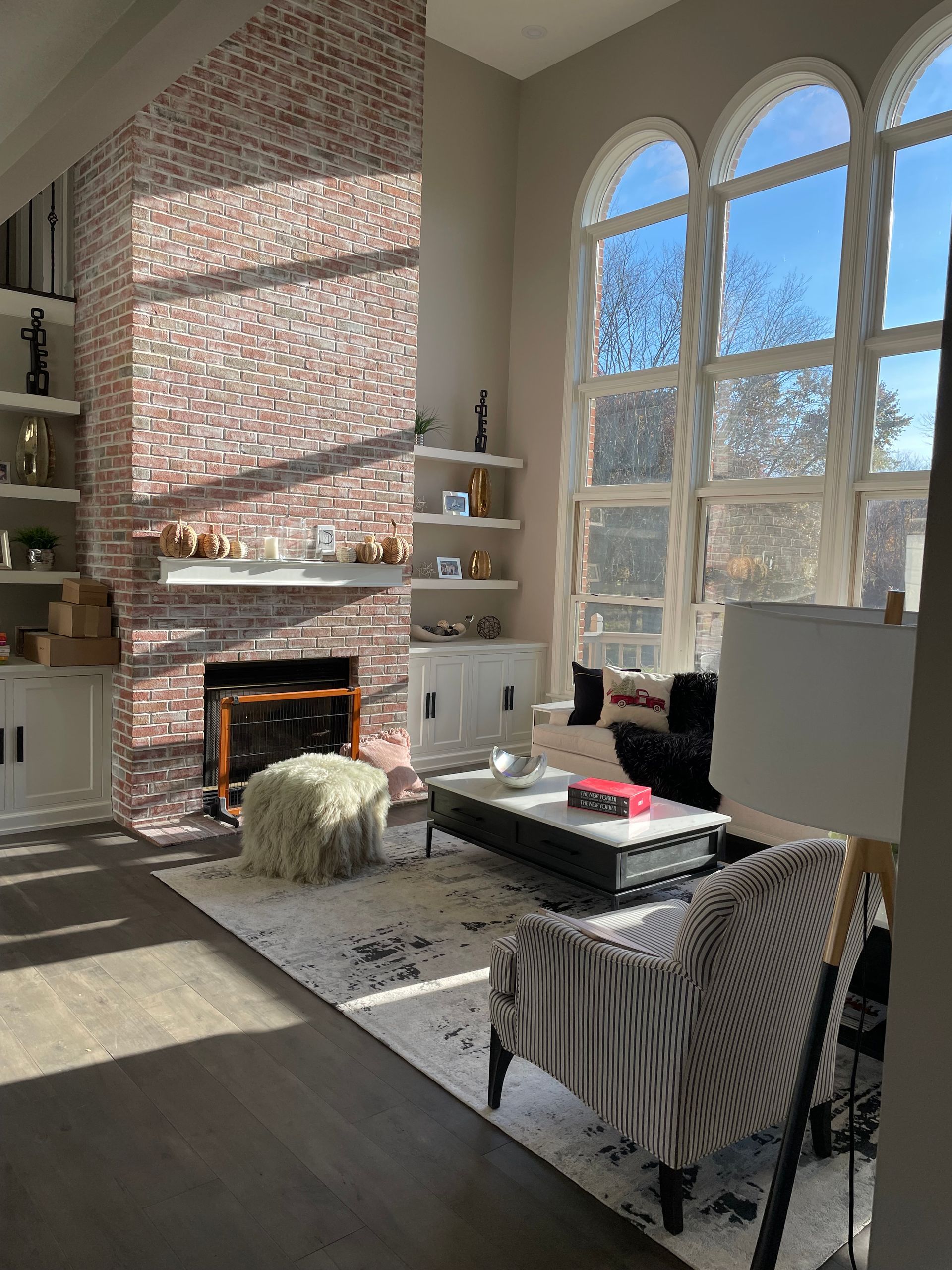 Sunlit living room with fireplace, large arched windows, and striped armchair by a coffee table.