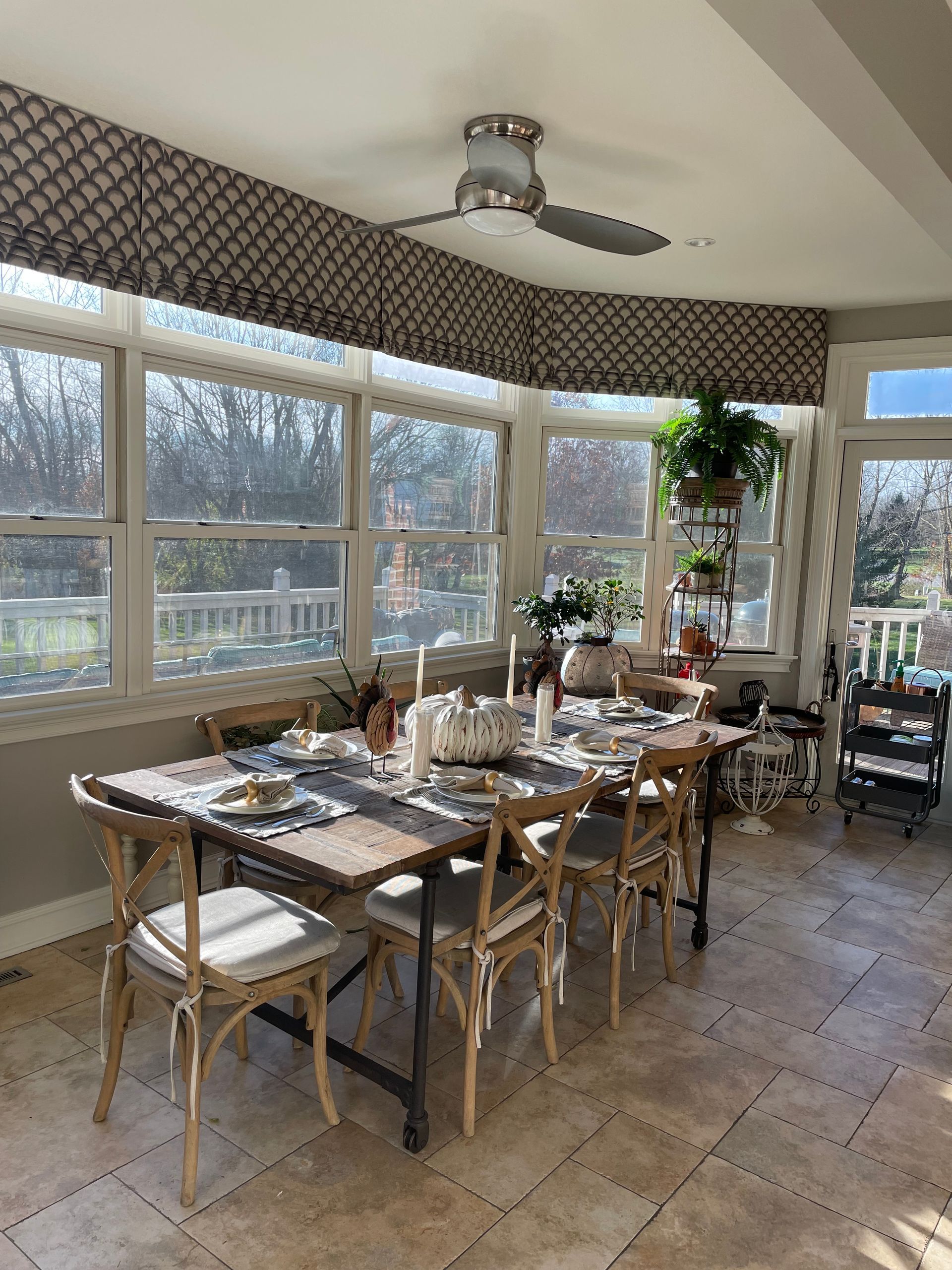 Bright sunroom dining area with a wooden table, chairs, large windows, and a ceiling fan.