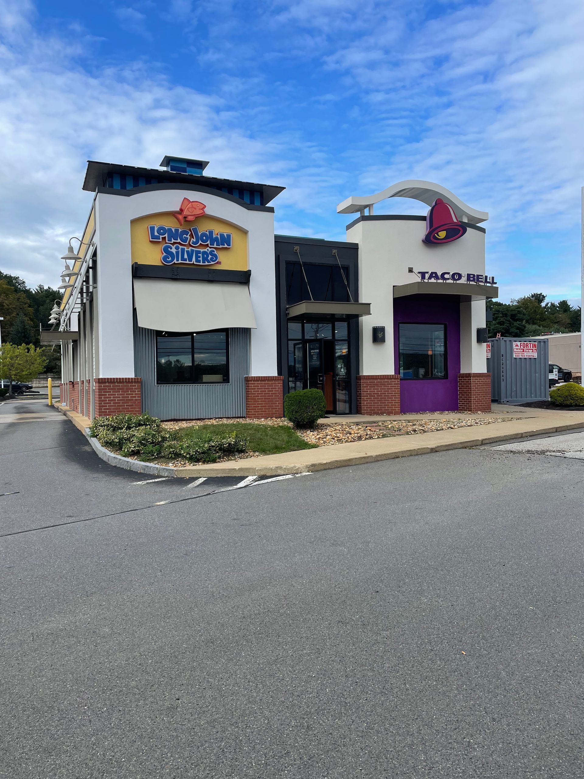 Two-story commercial building with colorful storefronts and a purple awning on a street corner under a blue sky