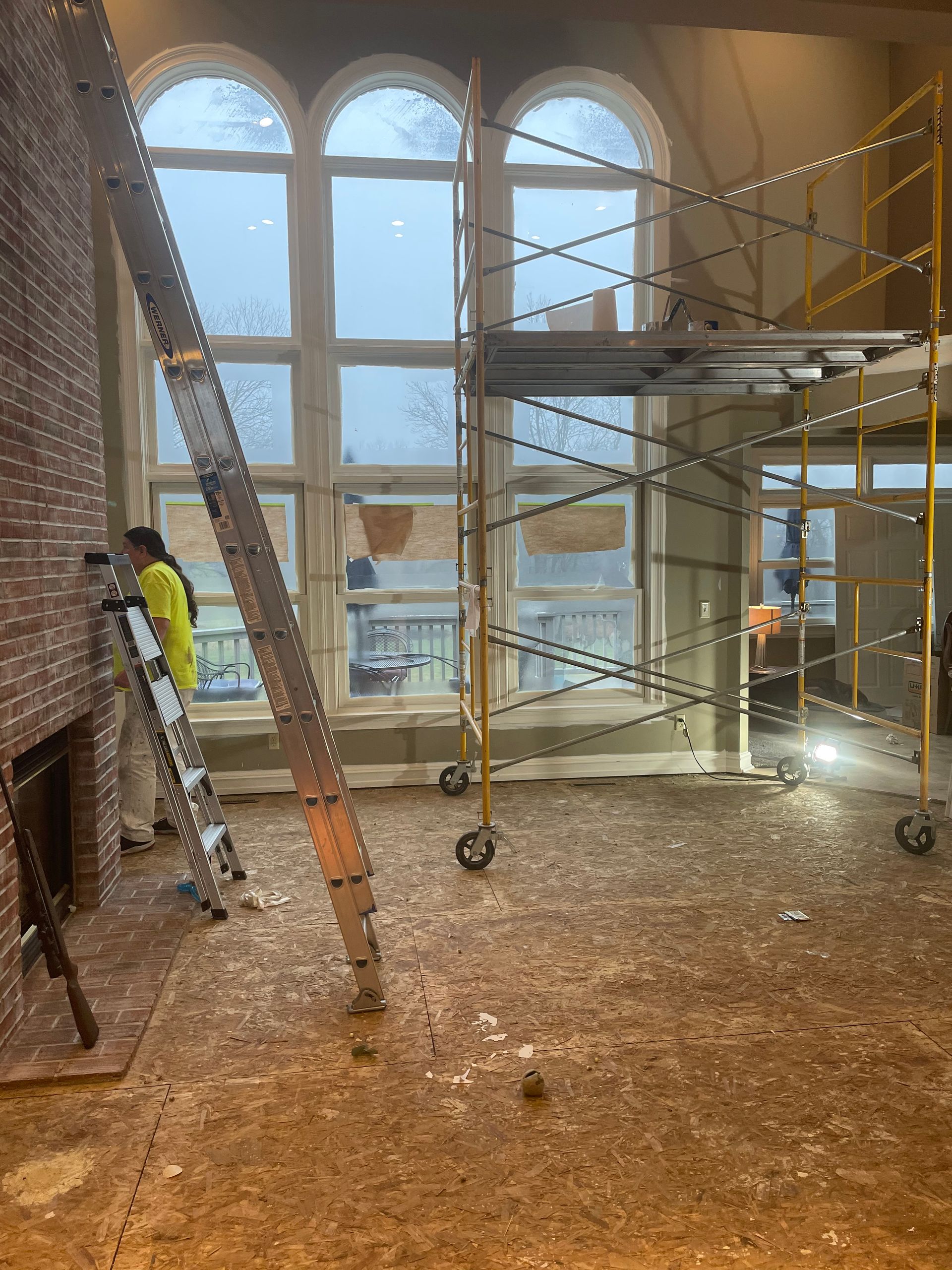 Scaffolded interior with large arched windows, brick walls, and a worker in a yellow vest on a dusty floor