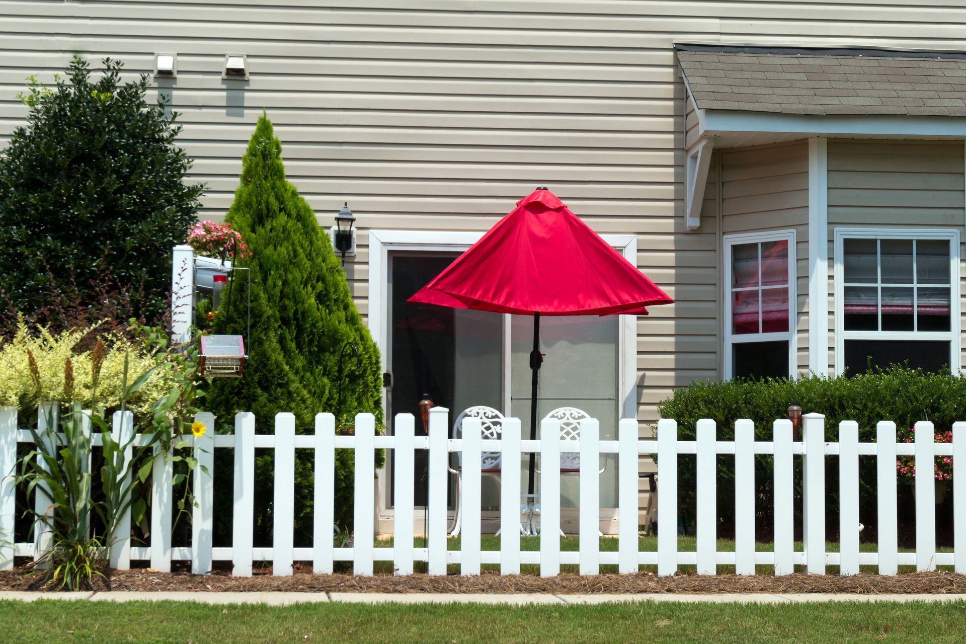 A white picket fence with a red umbrella in front of a house