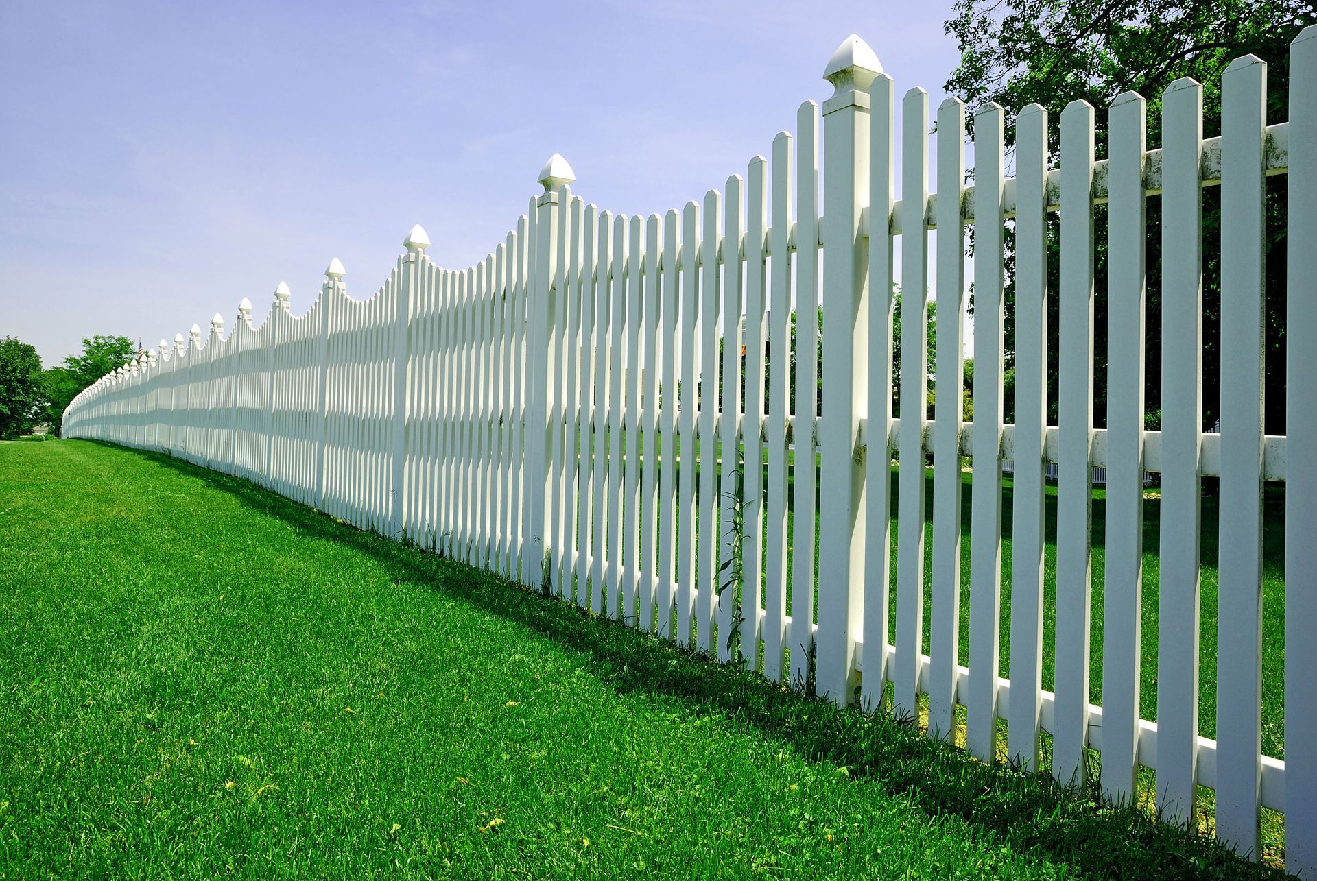 A long white picket fence surrounds a lush green field.